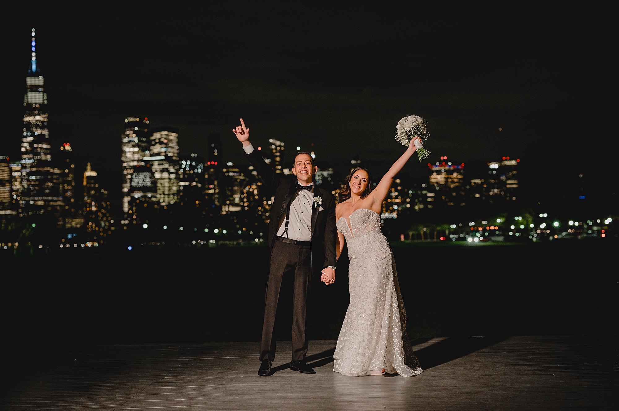bride and groom cheer standing in front of lit up NYC skyline