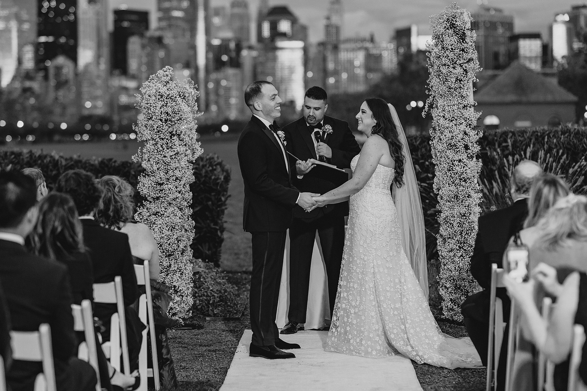 bride and groom hold hands between tall floral arrangements during the Liberty House wedding ceremony