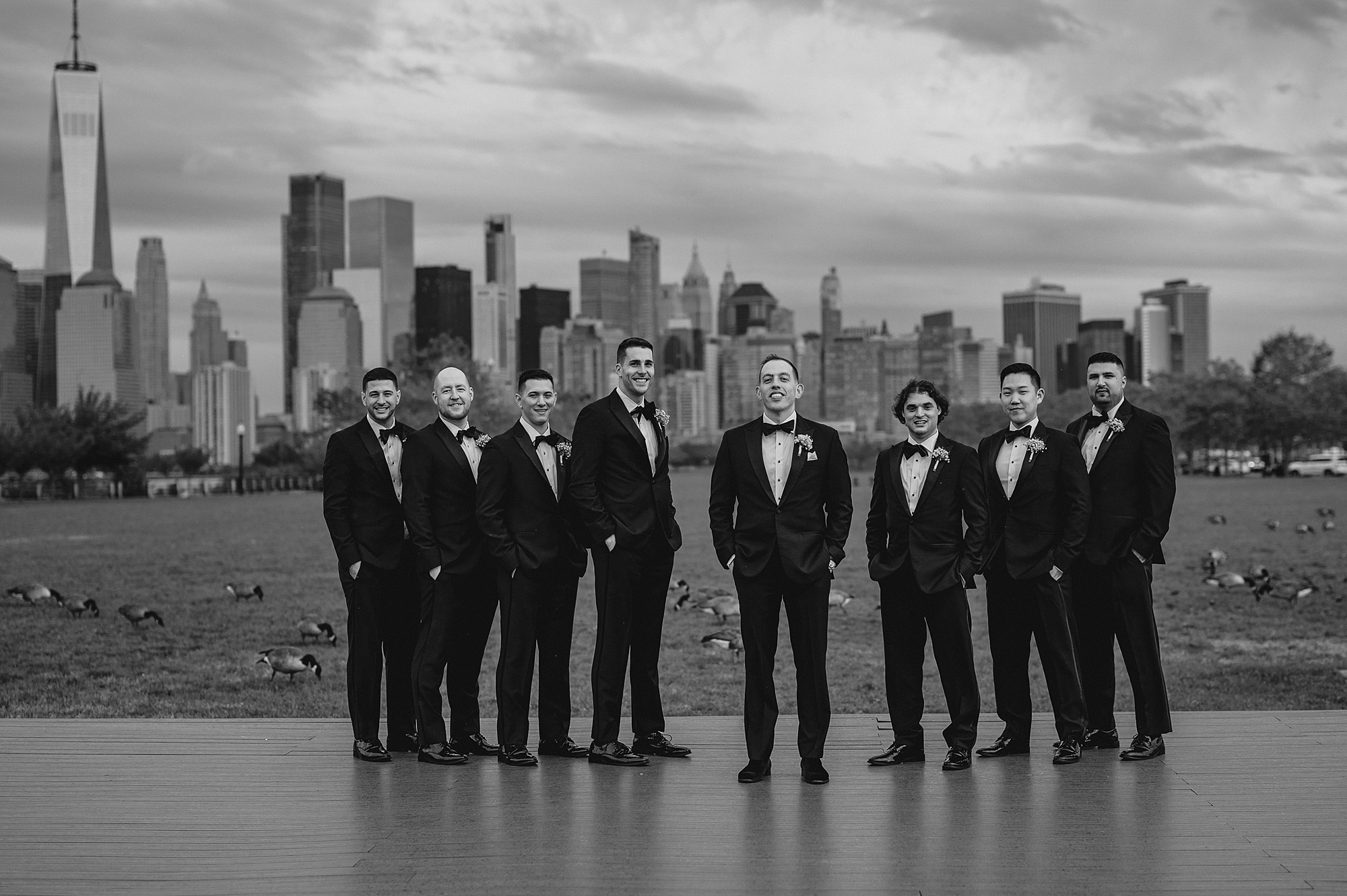 groom stands with groomsmen in black suits in front of Hudson River