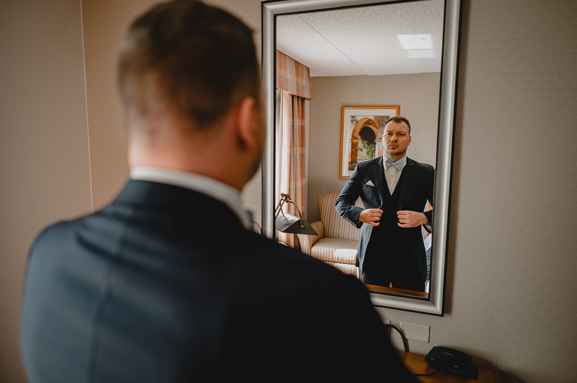 groom adjusts suit in mirror at the Garrison