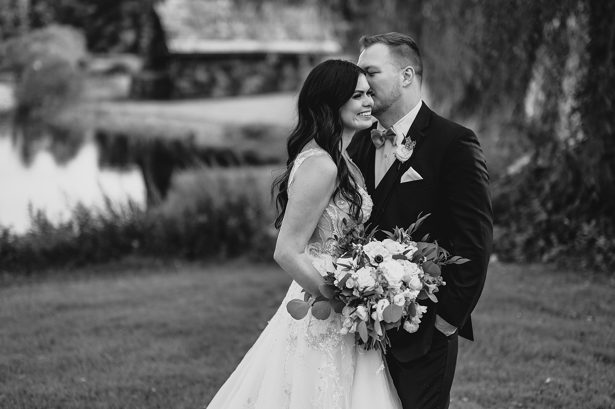 groom kisses bride's cheek in black and white photo