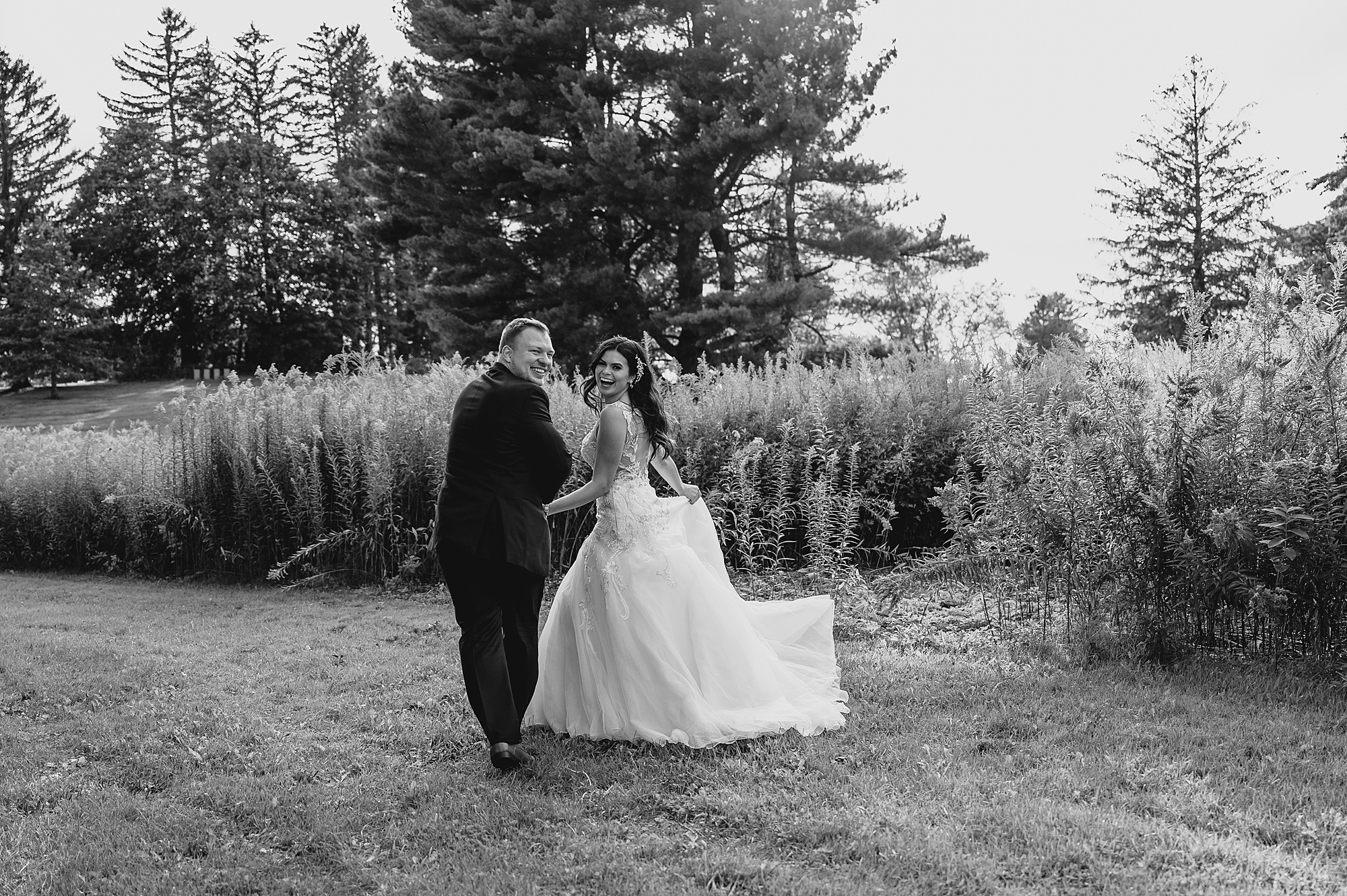 bride and groom walk towards field looking over shoulders