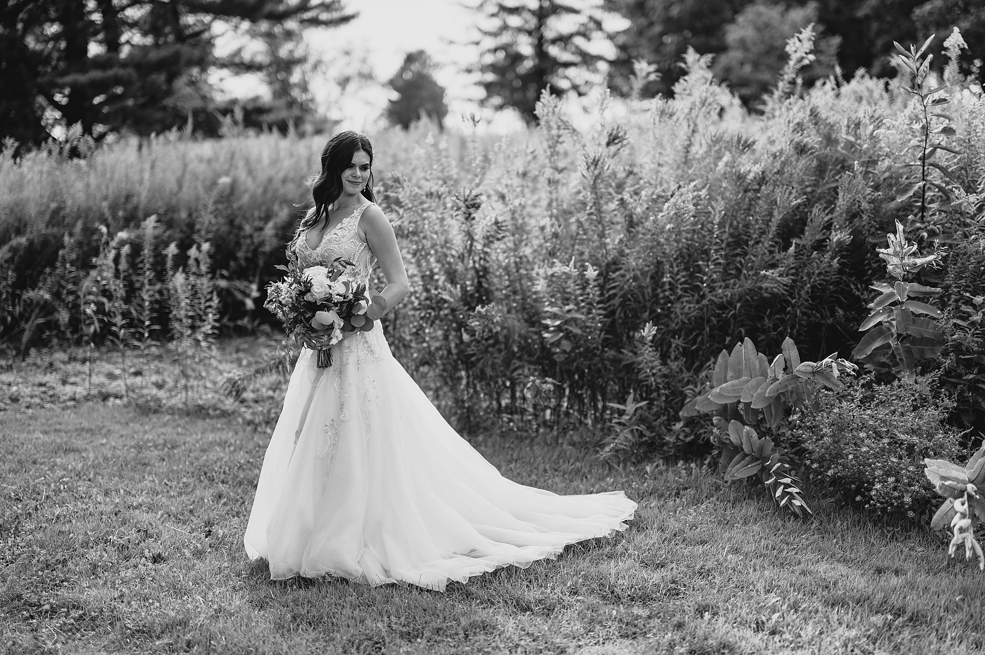 bride stands holding bouquet by tall field of grass at the Garrison
