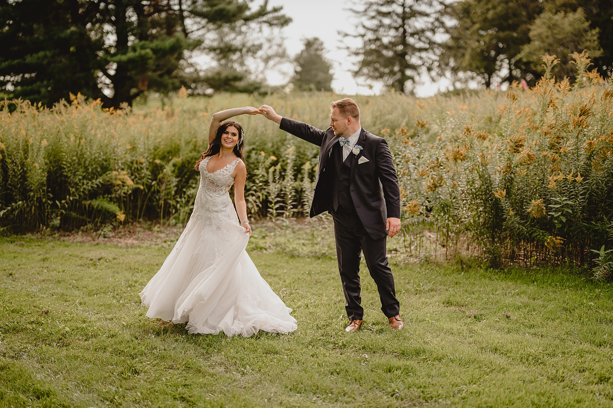 groom twirls bride by field on property at the Garrison
