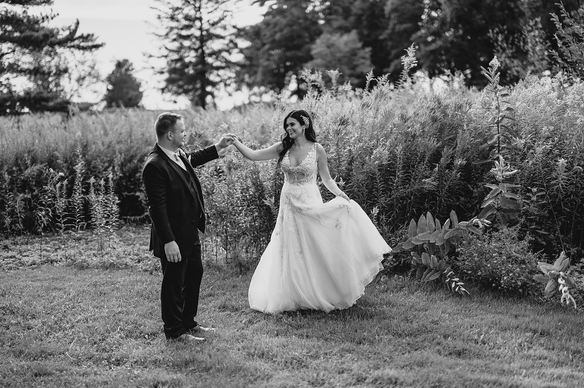 groom leads bride across field by tall grass at the Garrison