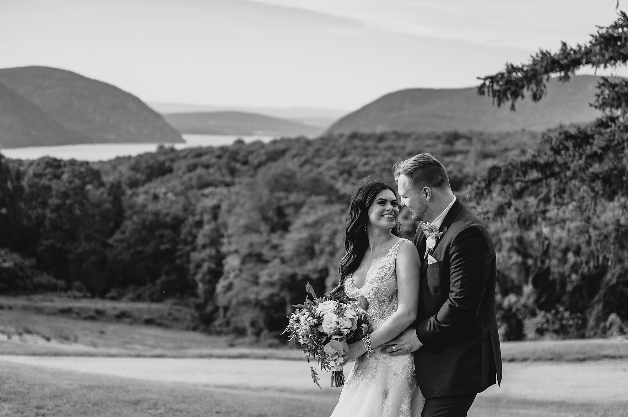 groom hugs bride from behind with mountains behind them at the Garrison