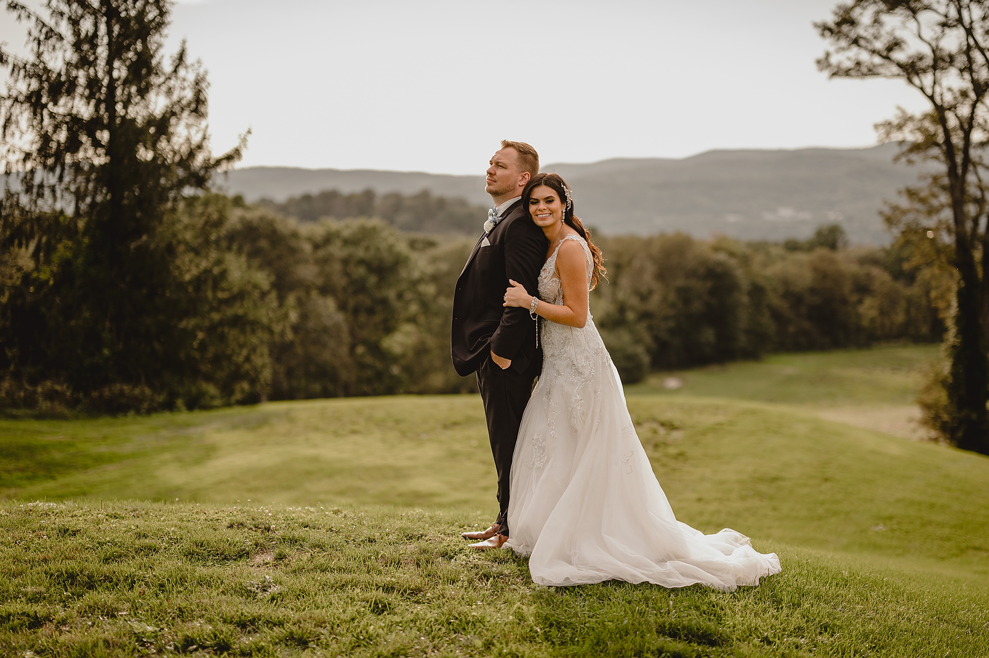 bride hugs groom from behind in front of mountains