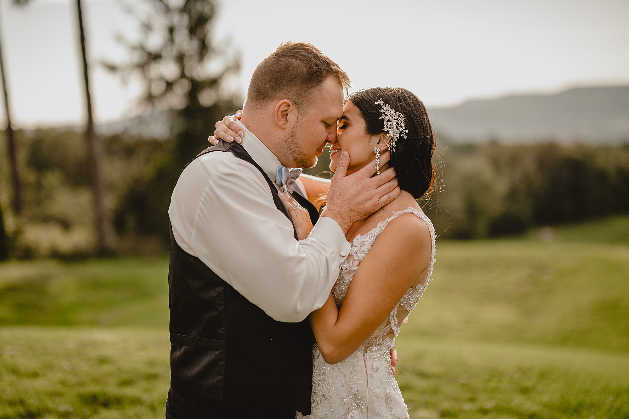 bride and groom lean heads together for a kiss in front of NY mountains