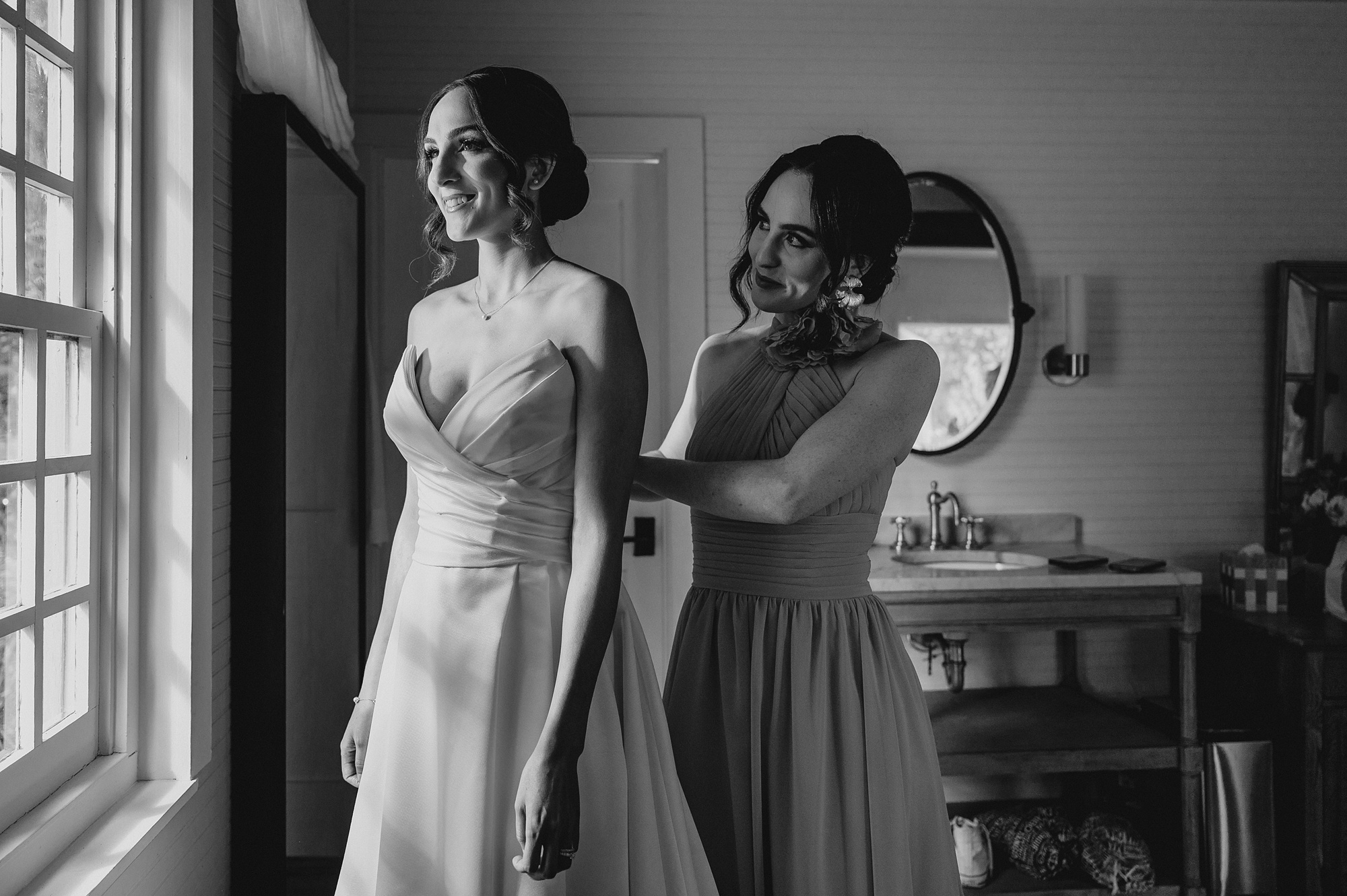 bridesmaid helps bride into wedding dress before NJ wedding day