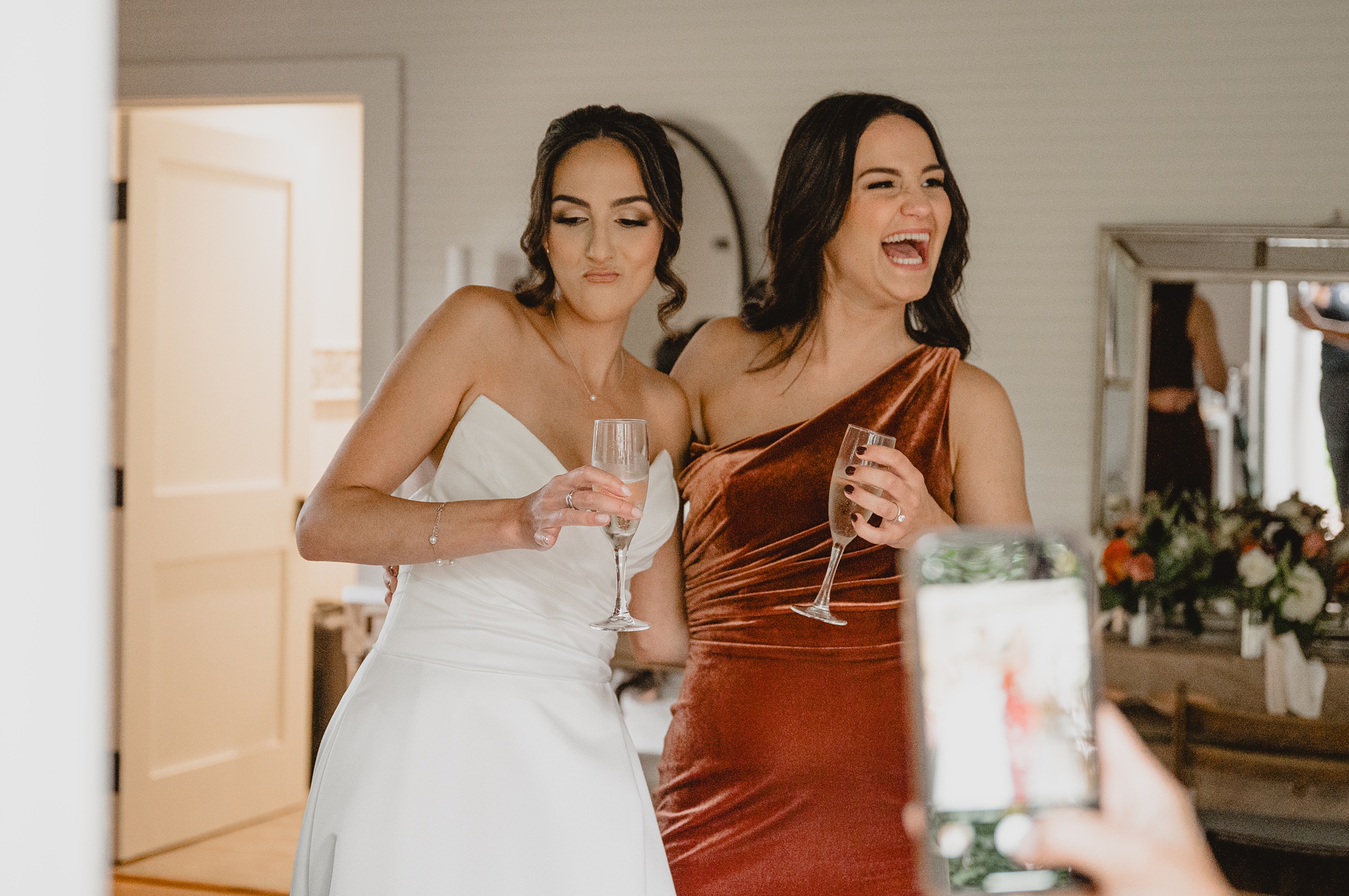 bride and bridesmaid laugh together drinking champagne 