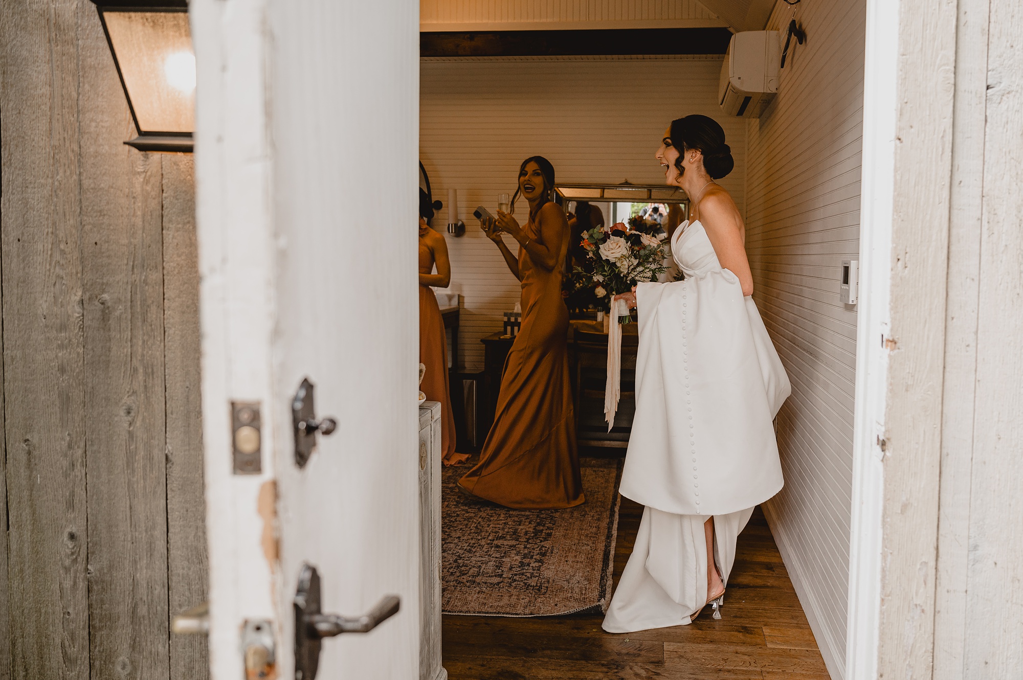 bride stands in hallway of Waterloo Village holding up wedding dress train in arms