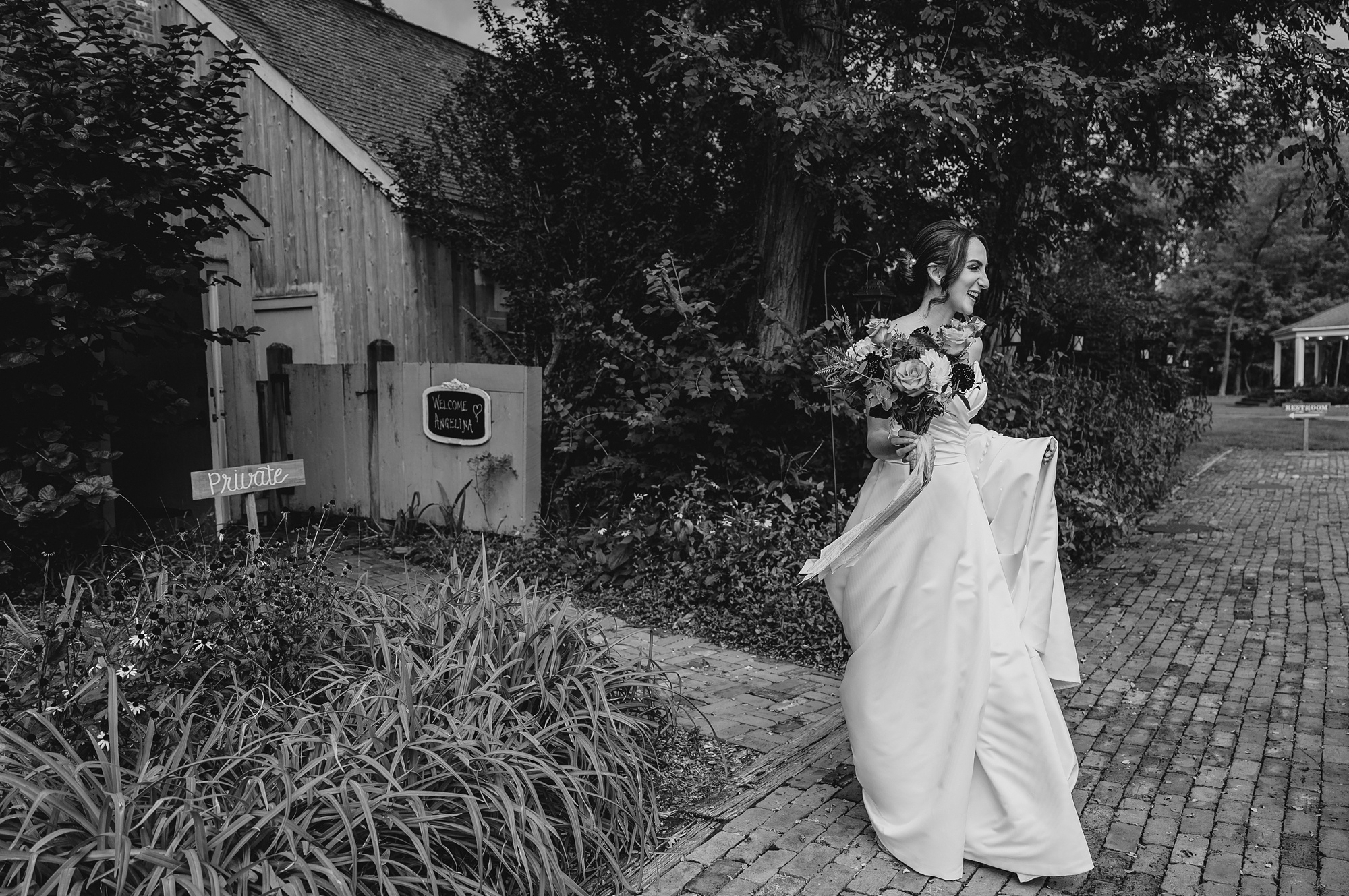 bride walks through garden outside Waterloo Village holding up skirt of wedding gown