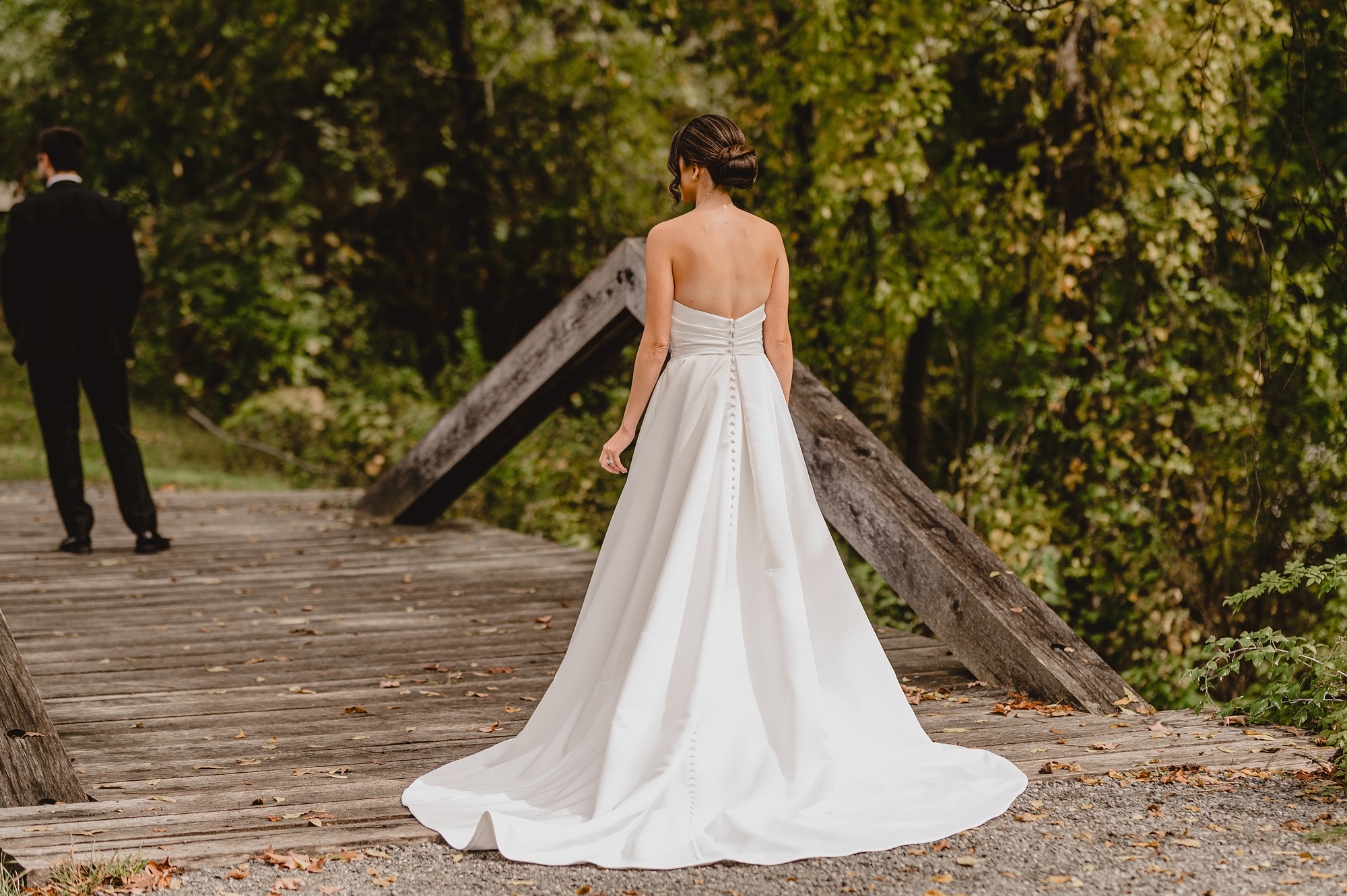 bride stands on bridge in strapless wedding gown to meet groom
