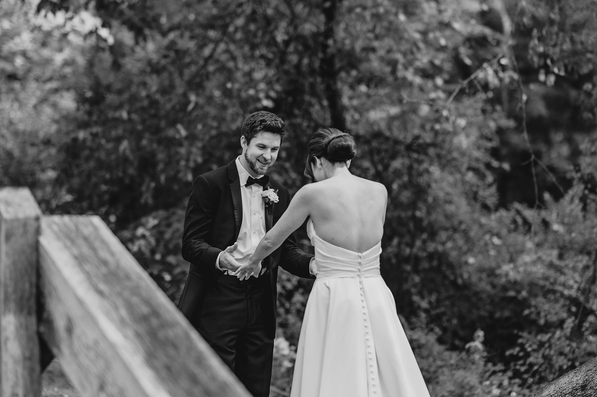 groom looks at bride in wedding dress during first look on bridge 