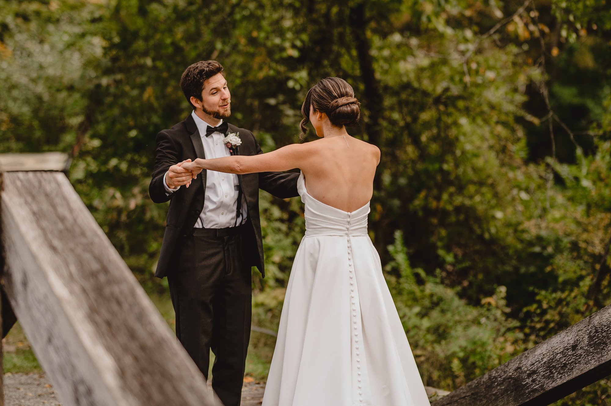 groom holds out bride's arms smiling at her during first look