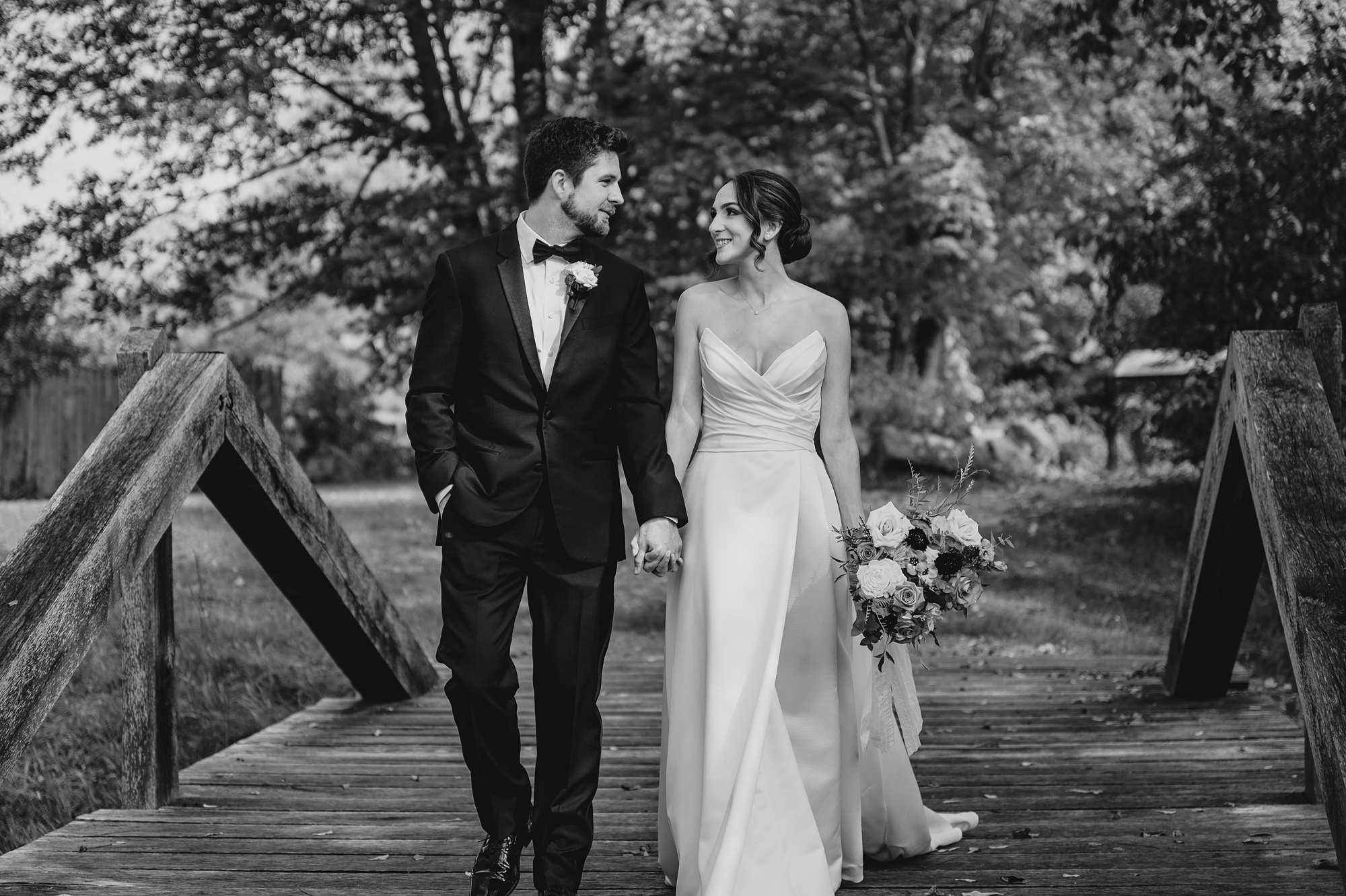 newlyweds hold hands walking across wooden bridge at Waterloo Village