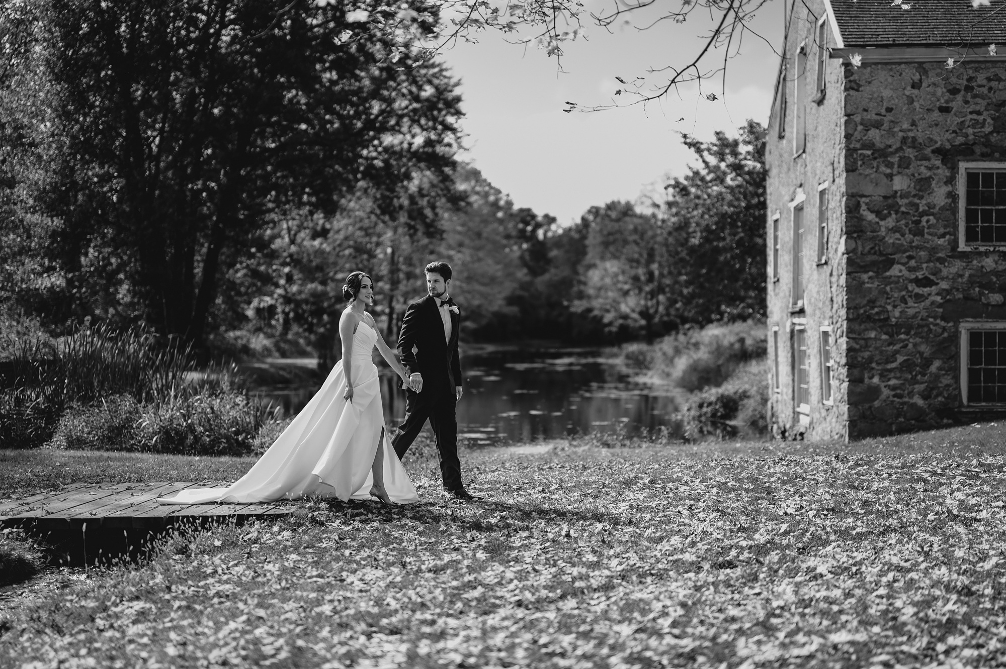 bride and groom hold hands walking towards stone barn