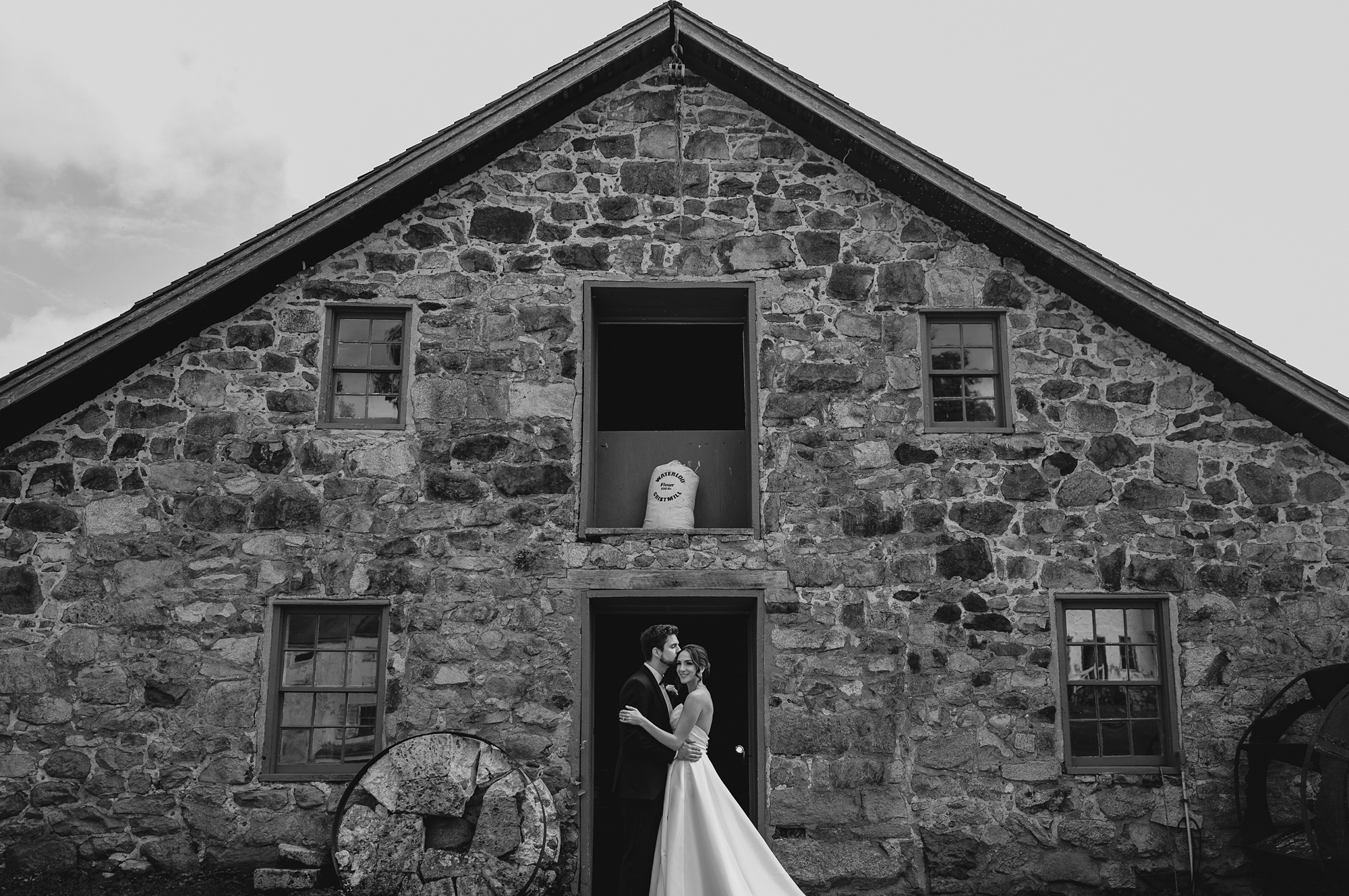 newlyweds hug in front of stone barn at Waterloo Village