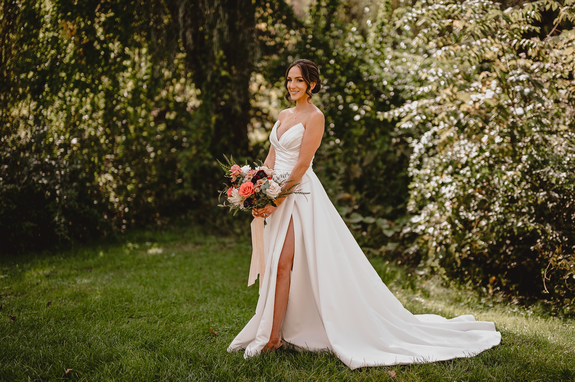 bride in strapless gown holds bouquet of pink flowers on lawn at Waterloo Village