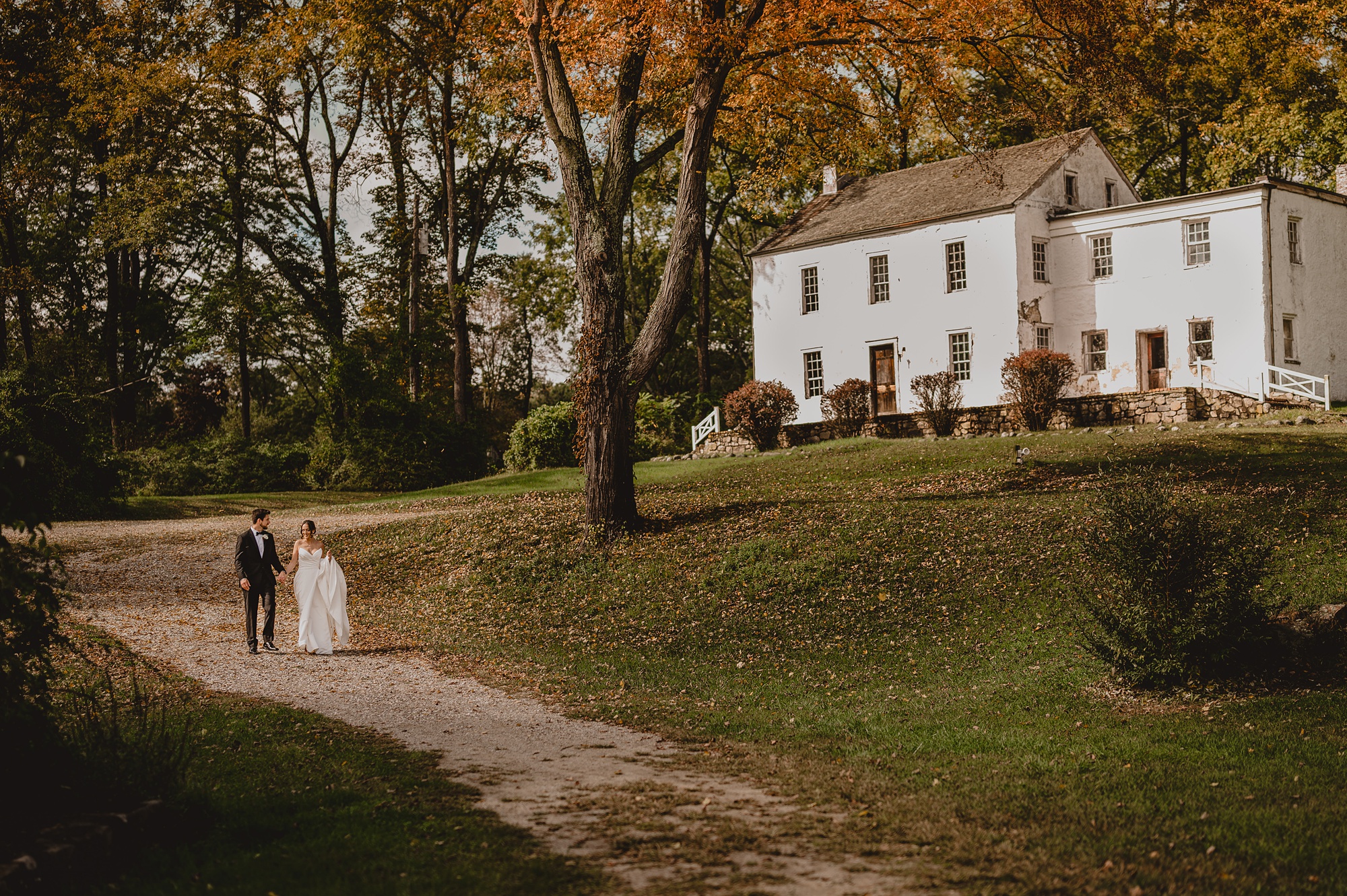 newlyweds hold hands walking under fall trees 