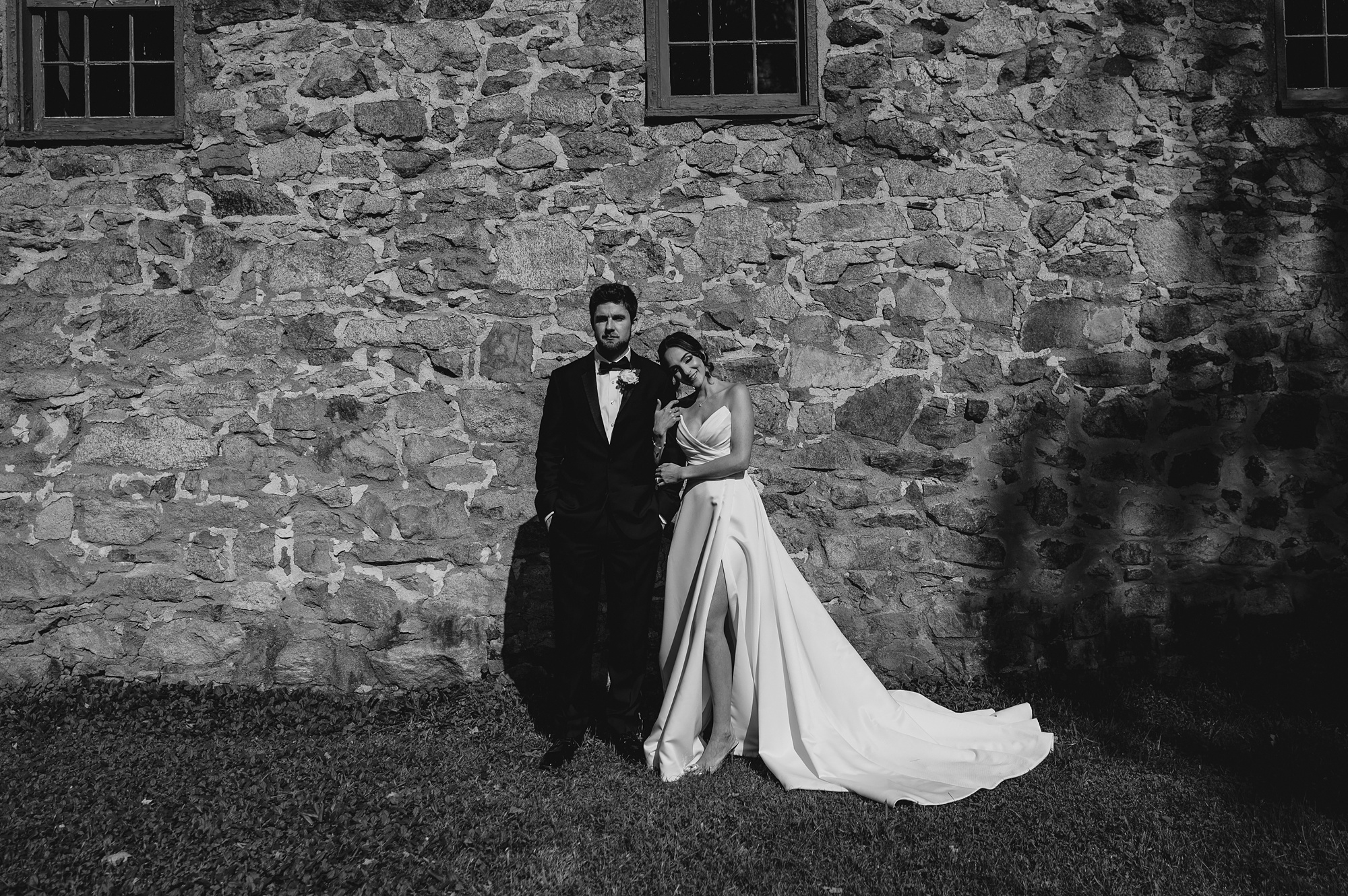 bride leans head on groom's shoulder in front of stone barn