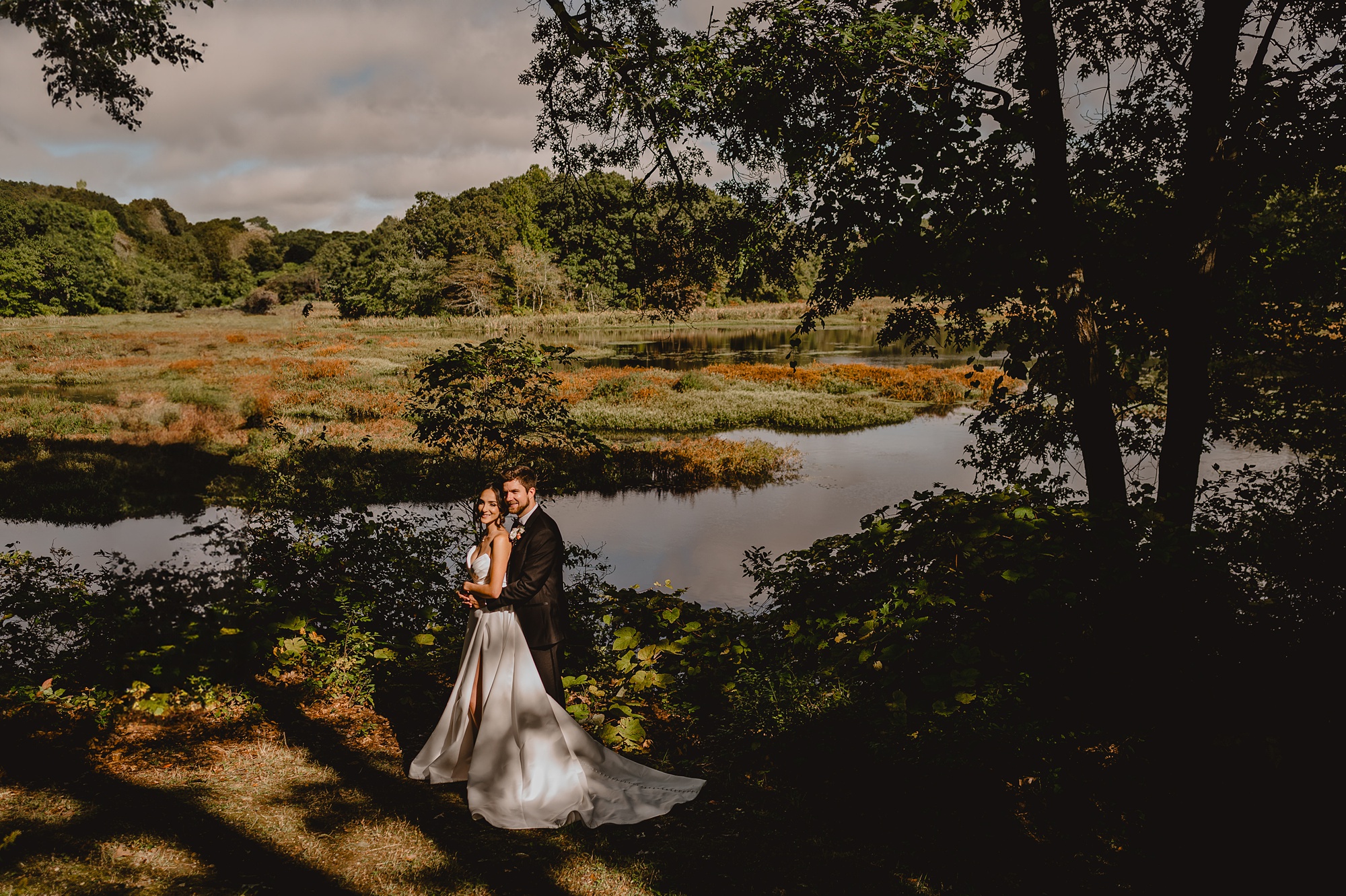 newlyweds hug near pond at Waterloo Village in the shadows 