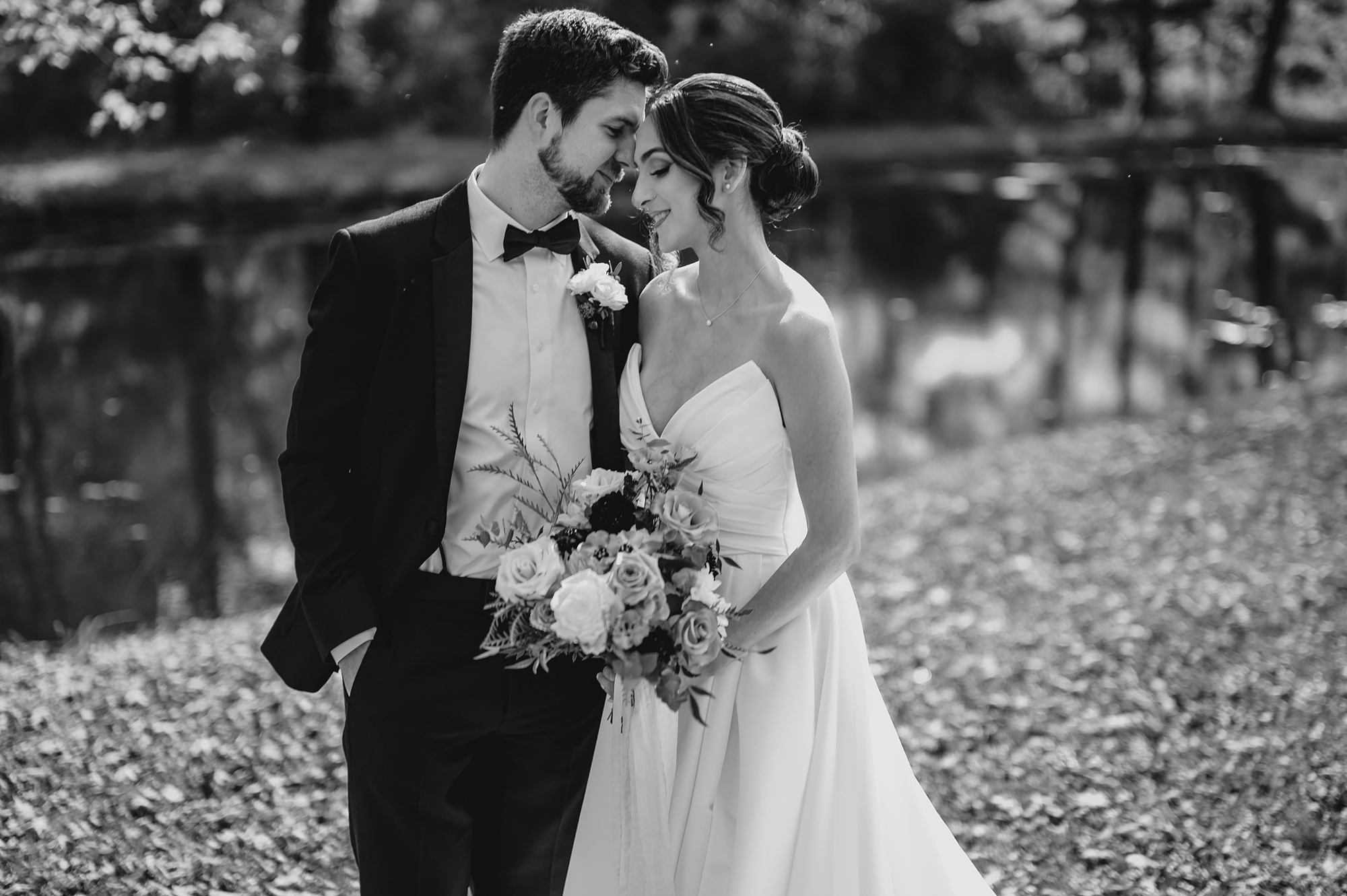 groom kisses bride's cheek near pond at Waterloo Village