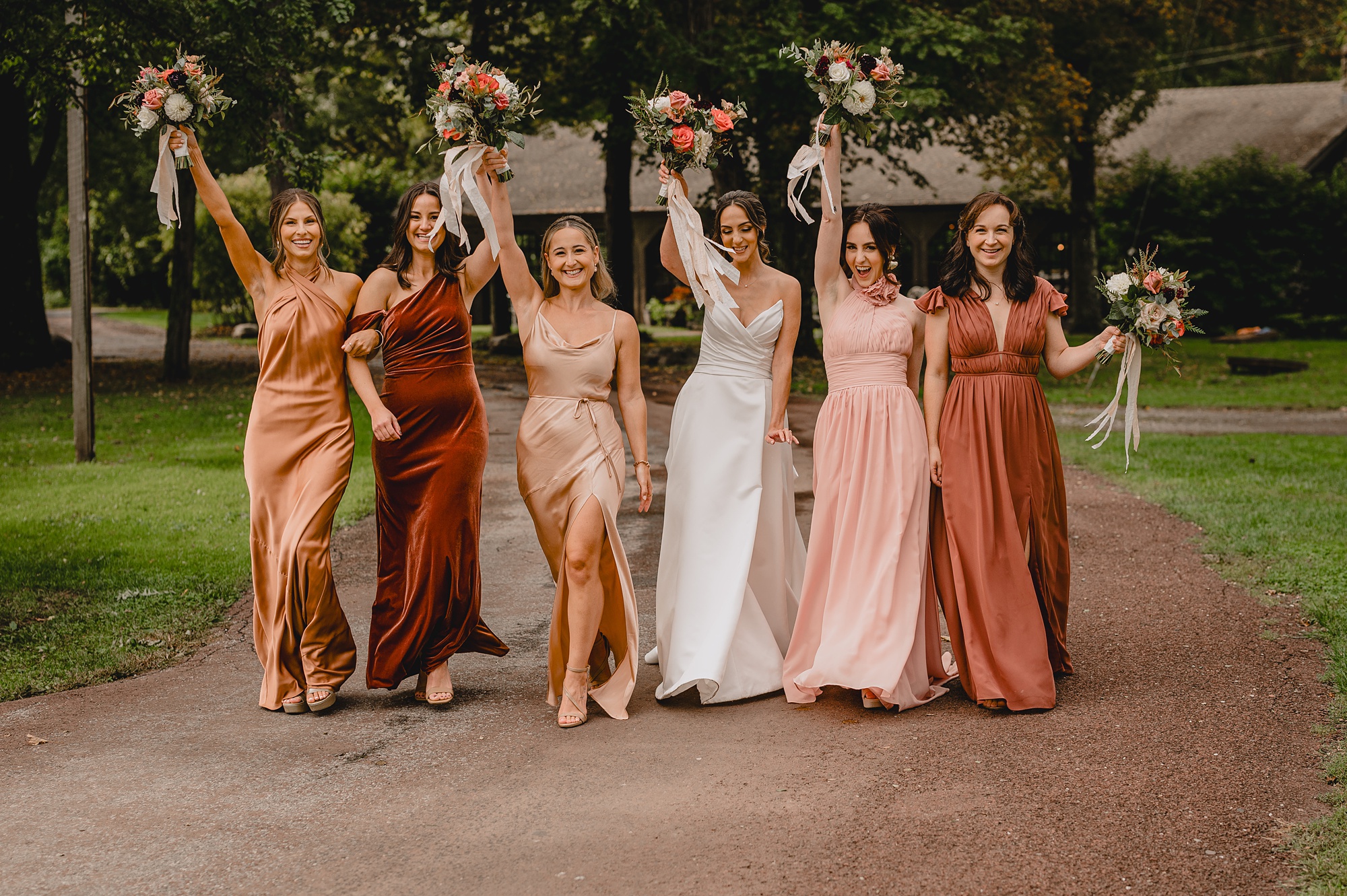 bride and bridesmaids in mismatched pink gowns cheer lifting bouquets in the air