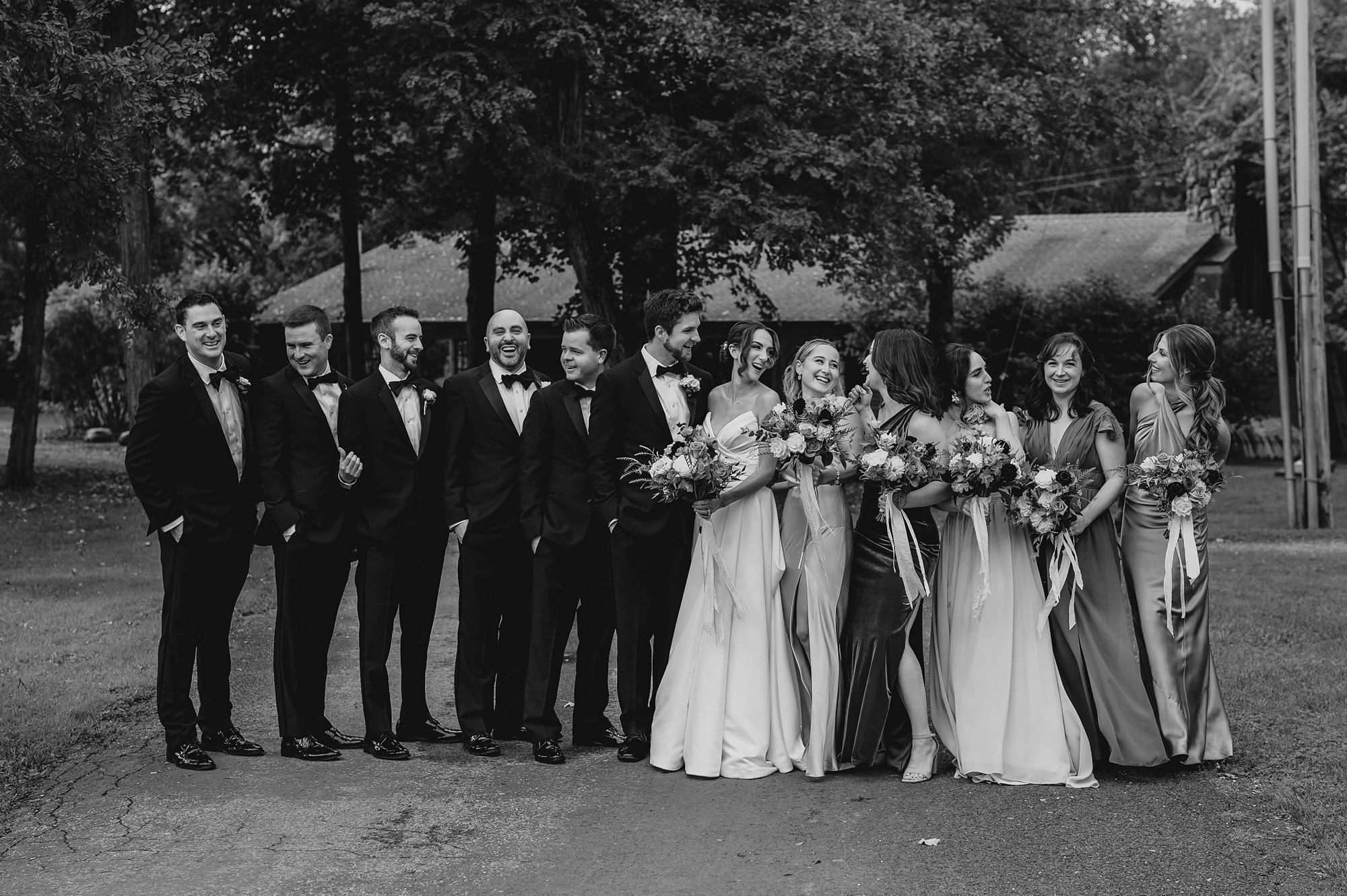 groom looks at bride with wedding party around them 