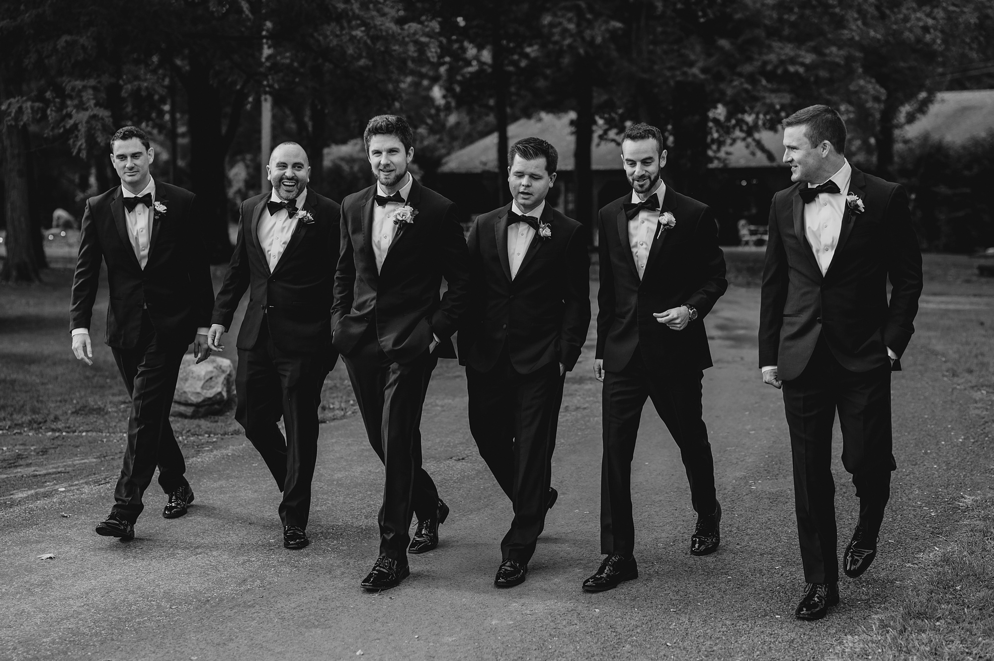 groom and groomsmen walk in black tuxes on walkway at Waterloo Village
