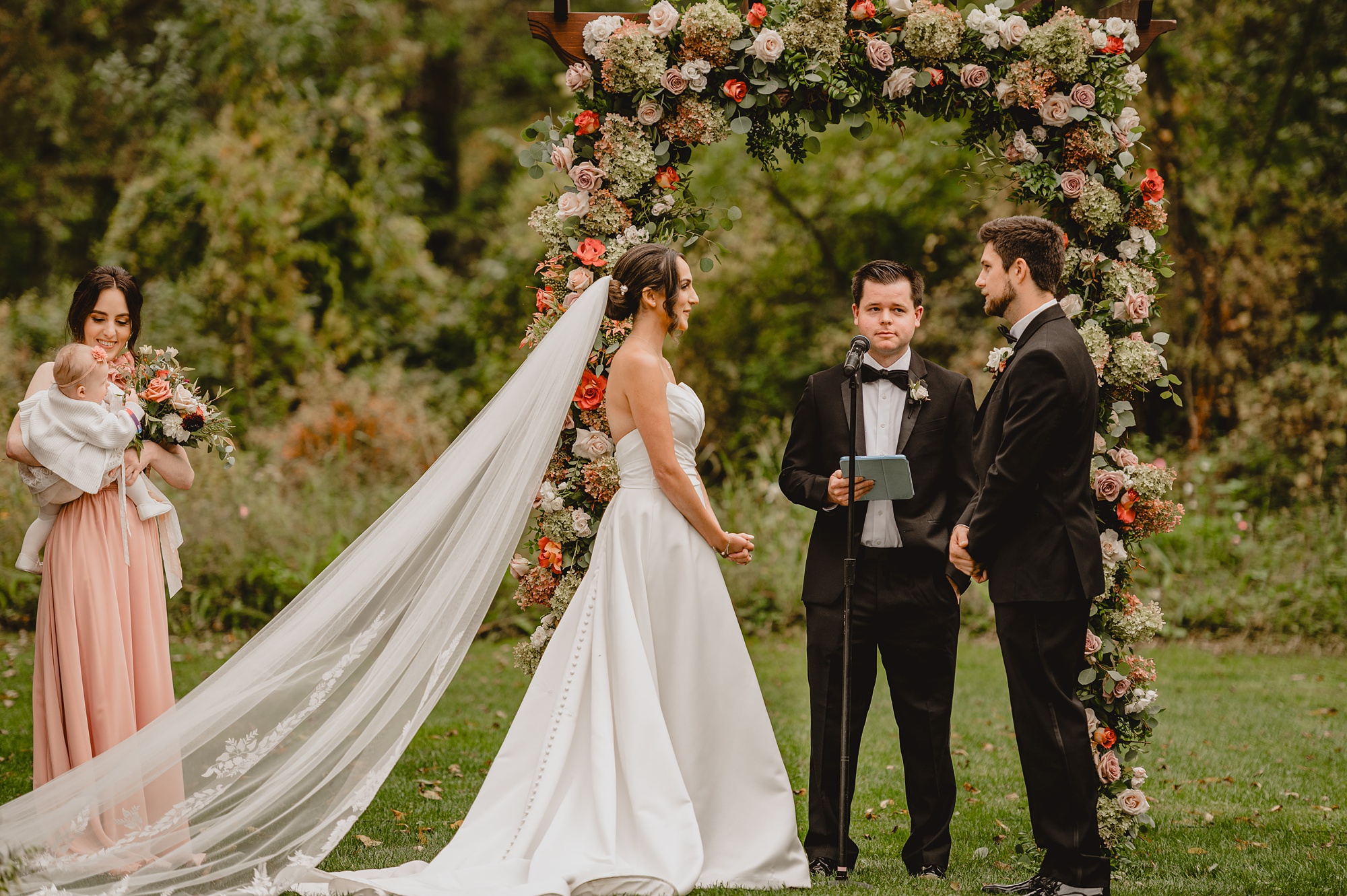 newlyweds exchange vows under arbor covered in flowers at Waterloo Village