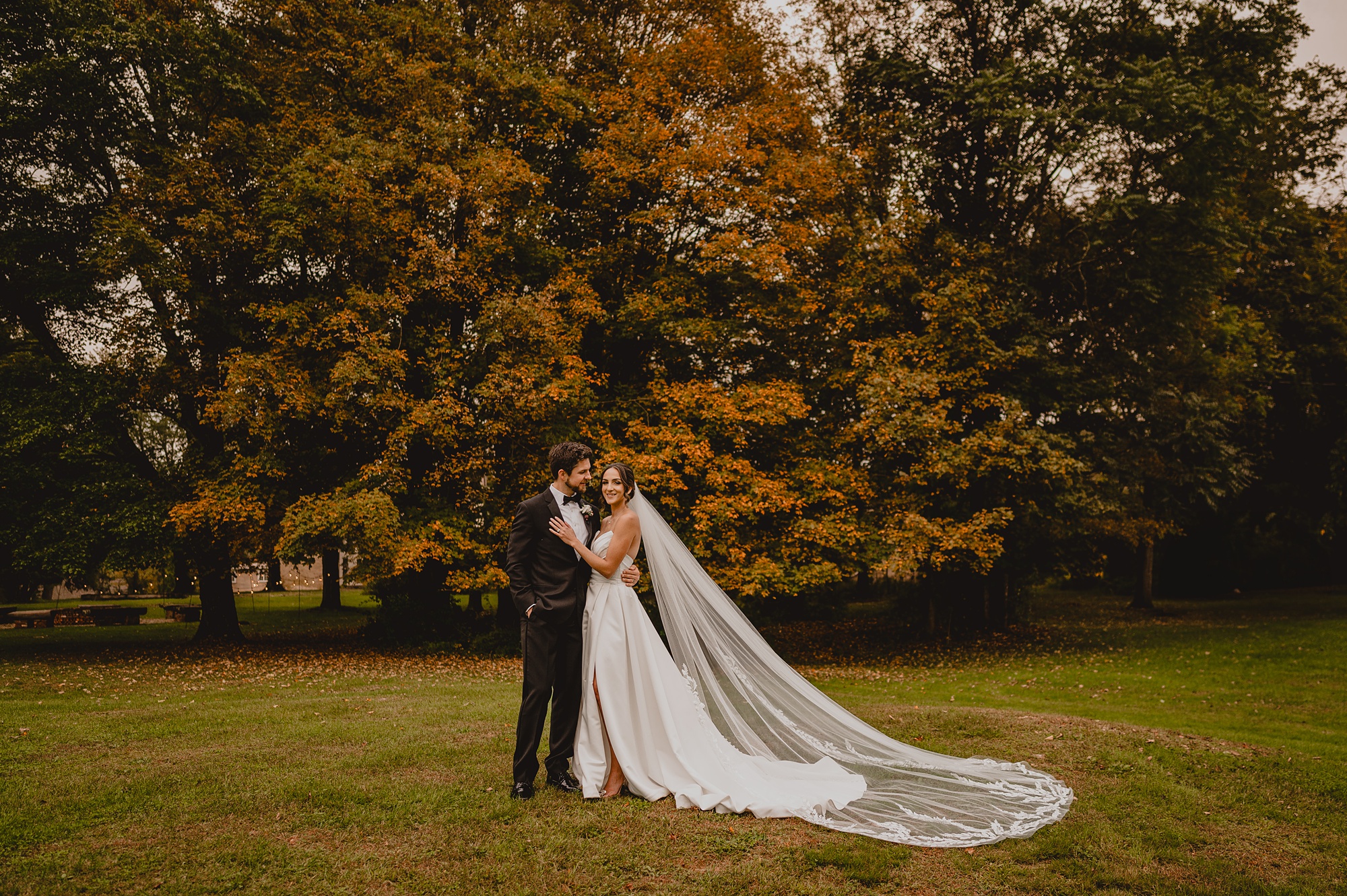 newlyweds hug under orange leaves of tree on property at Waterloo Village