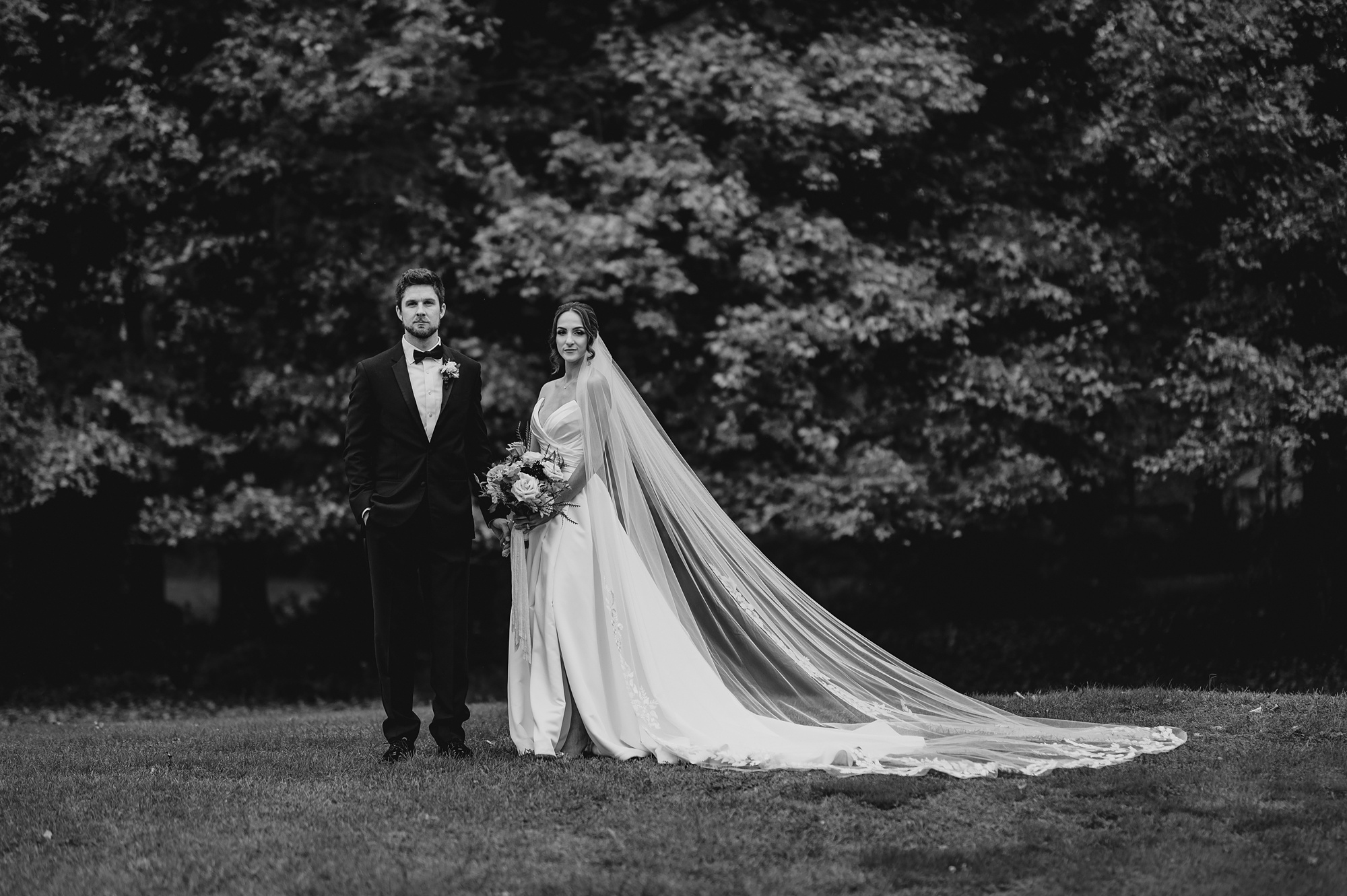 bride and groom stand together on lawn at Waterloo Village with bride's veil draped behind them