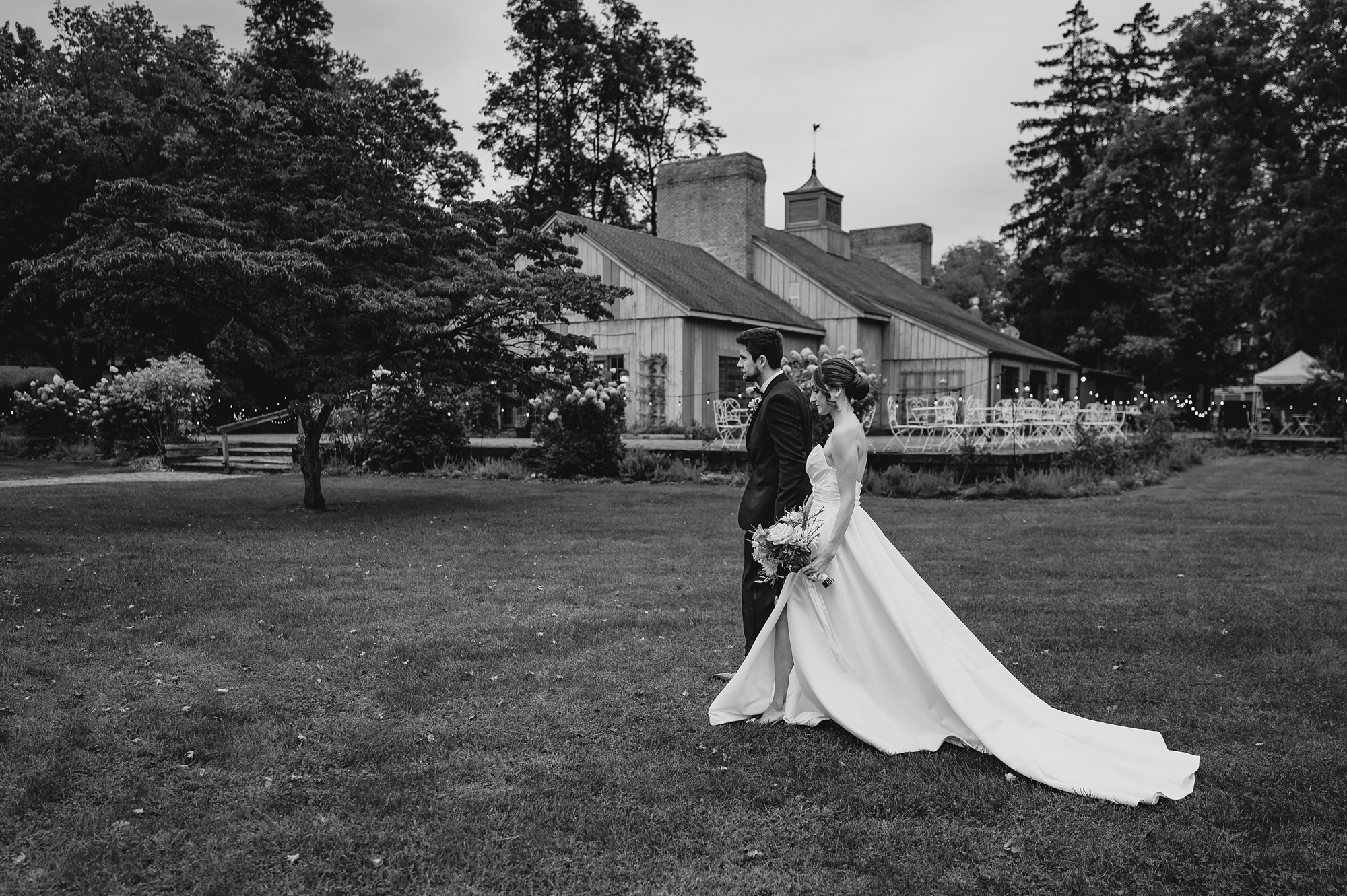 newlyweds hold hands walking across lawn outside Waterloo Village