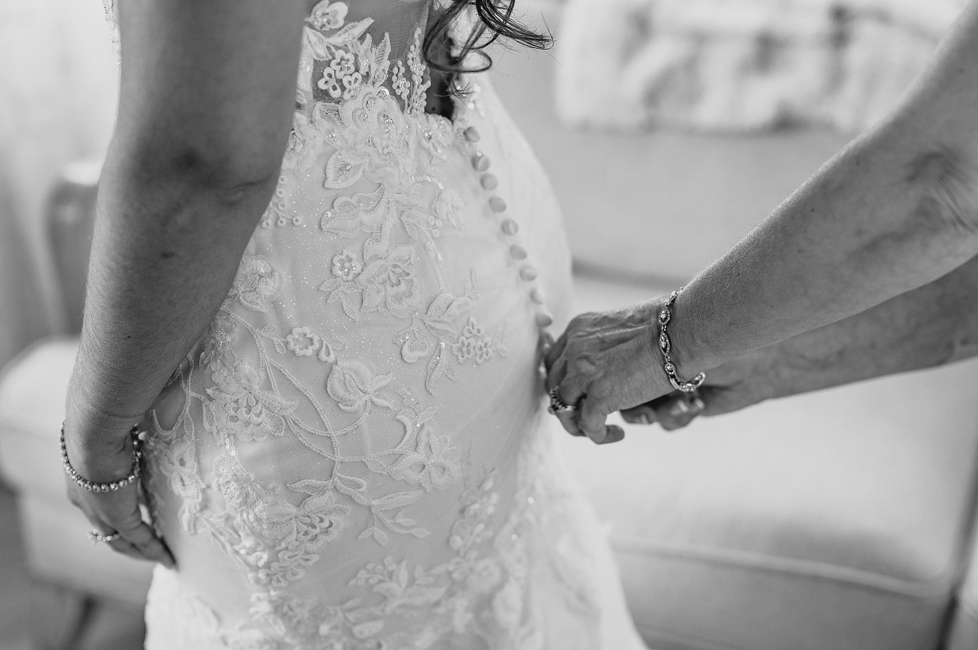 woman buttons up back of wedding dress for bride