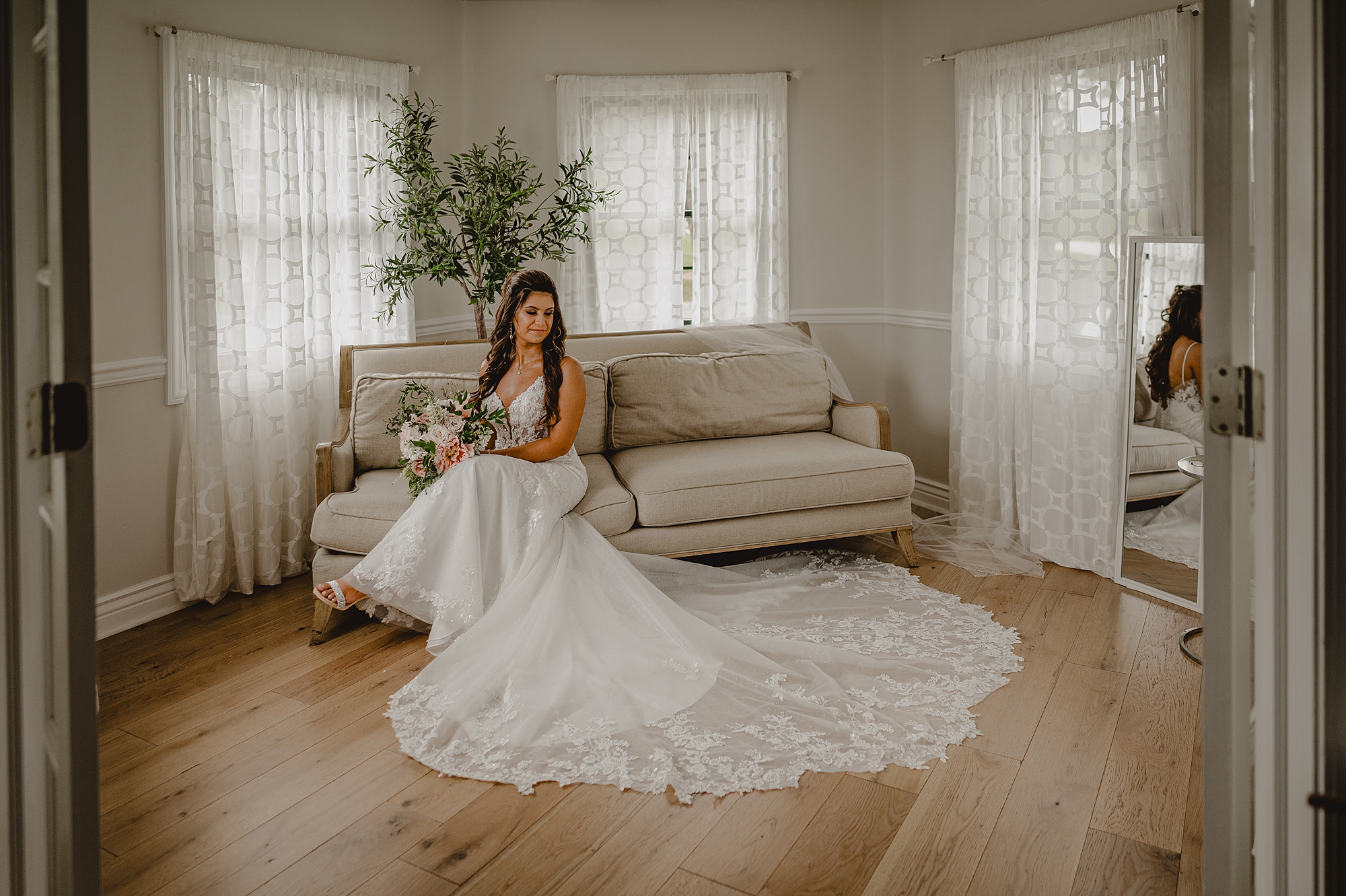 bride sits on tan sofa with lace train of skirt around her