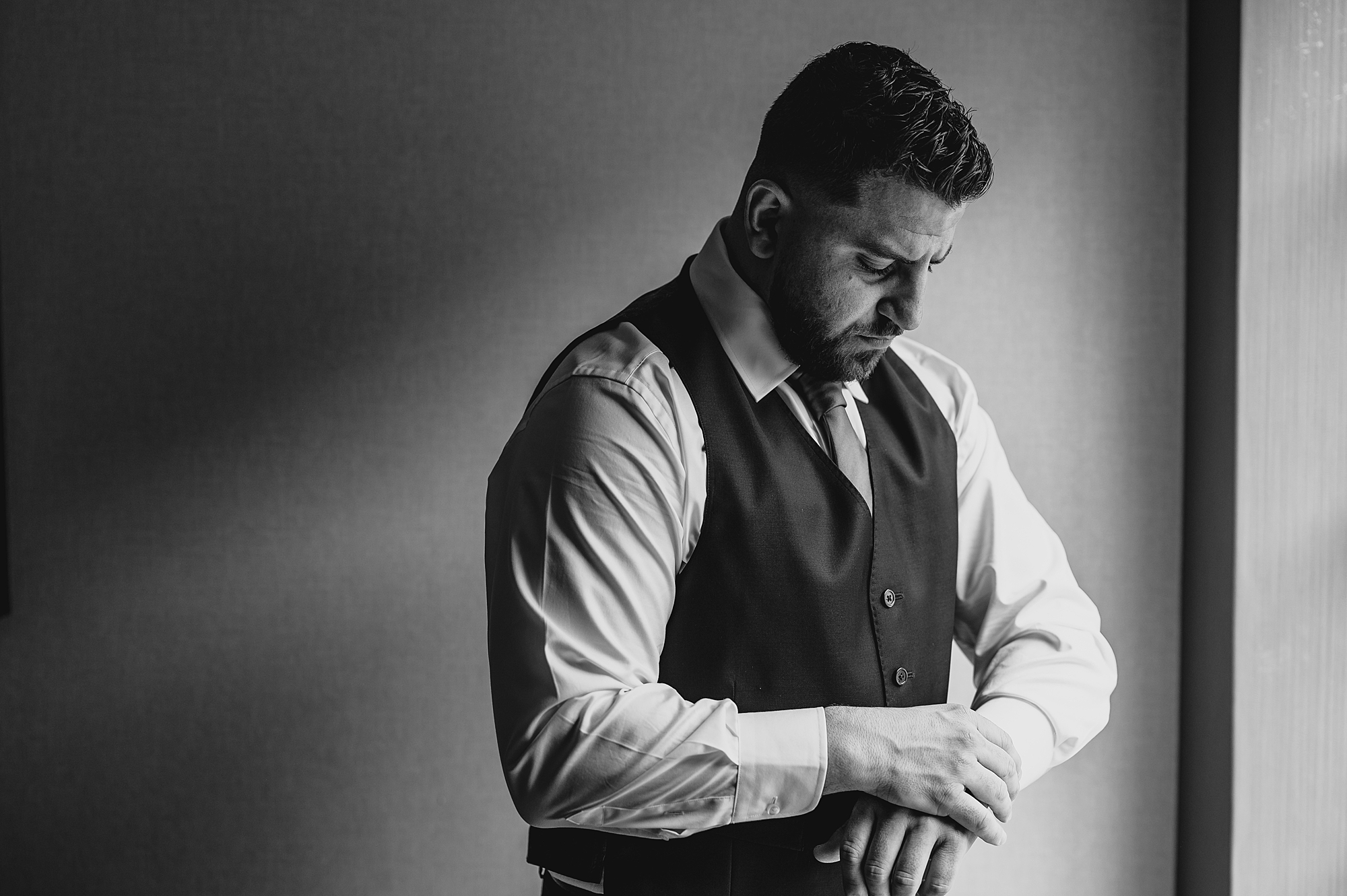 groom adjusts cufflinks in front of window at Skyview Golf Club