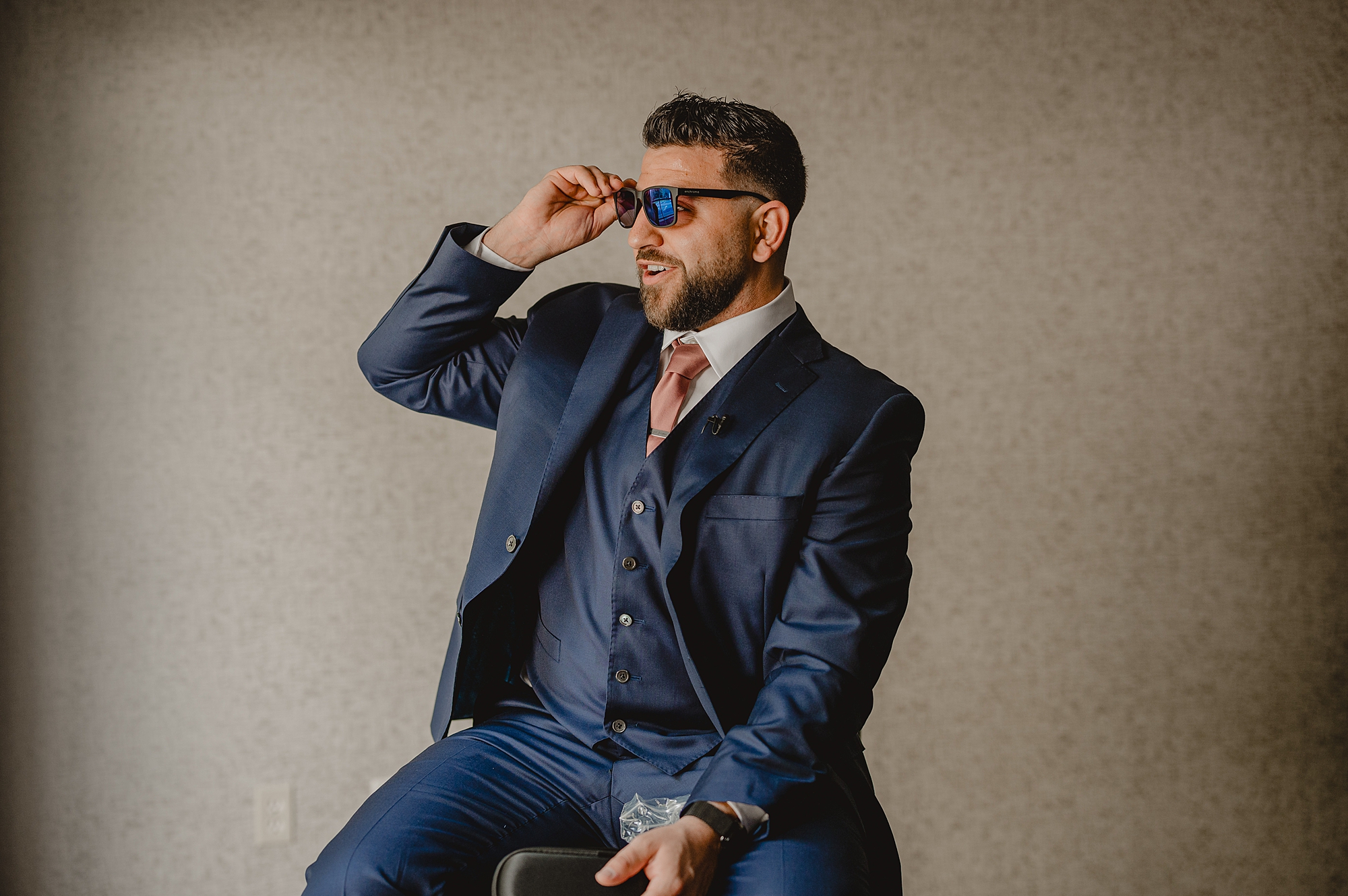 groom lifts up sunglasses laughing sitting on stool