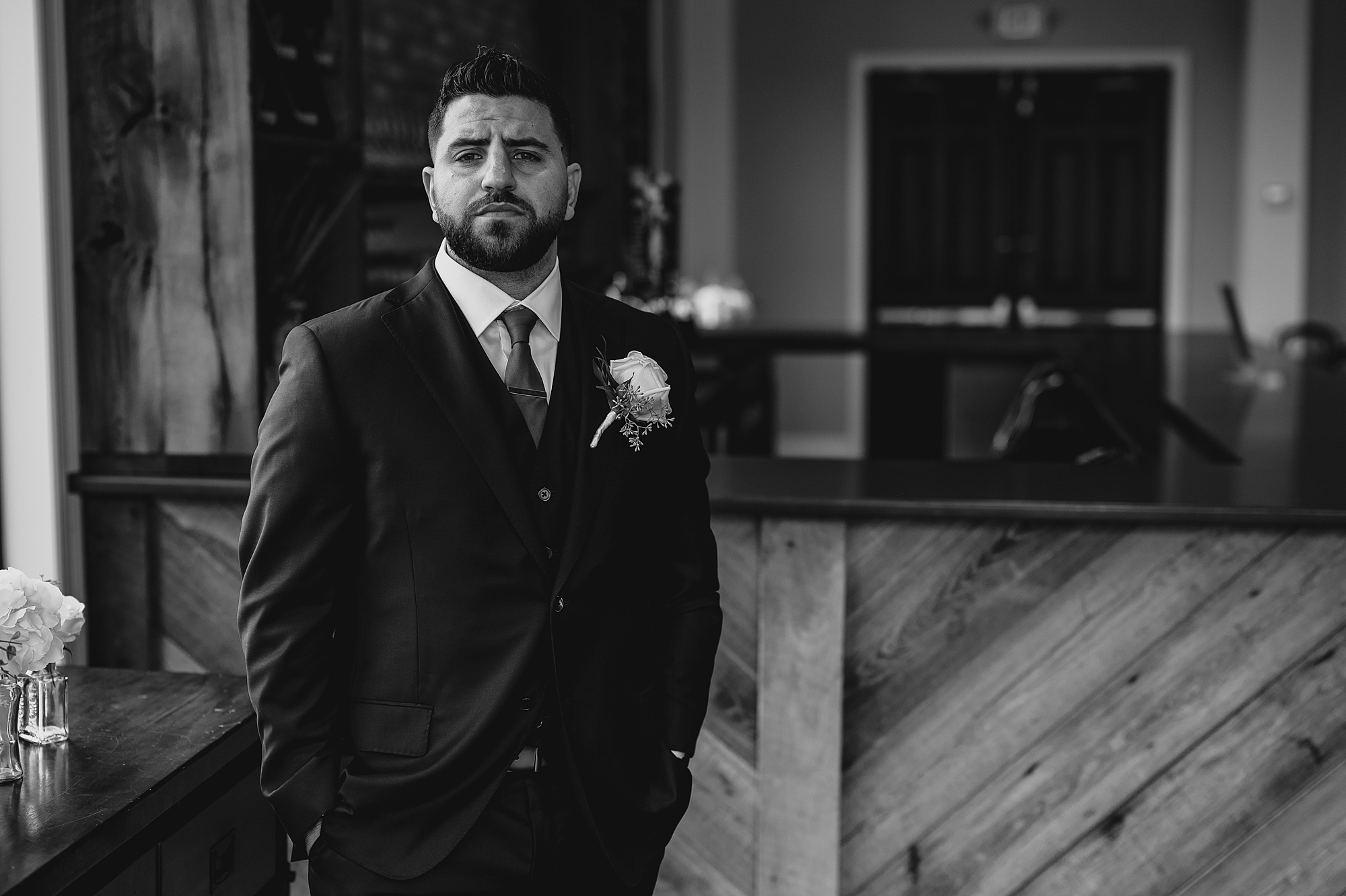 groom stands on patio in suit looking out on lawn