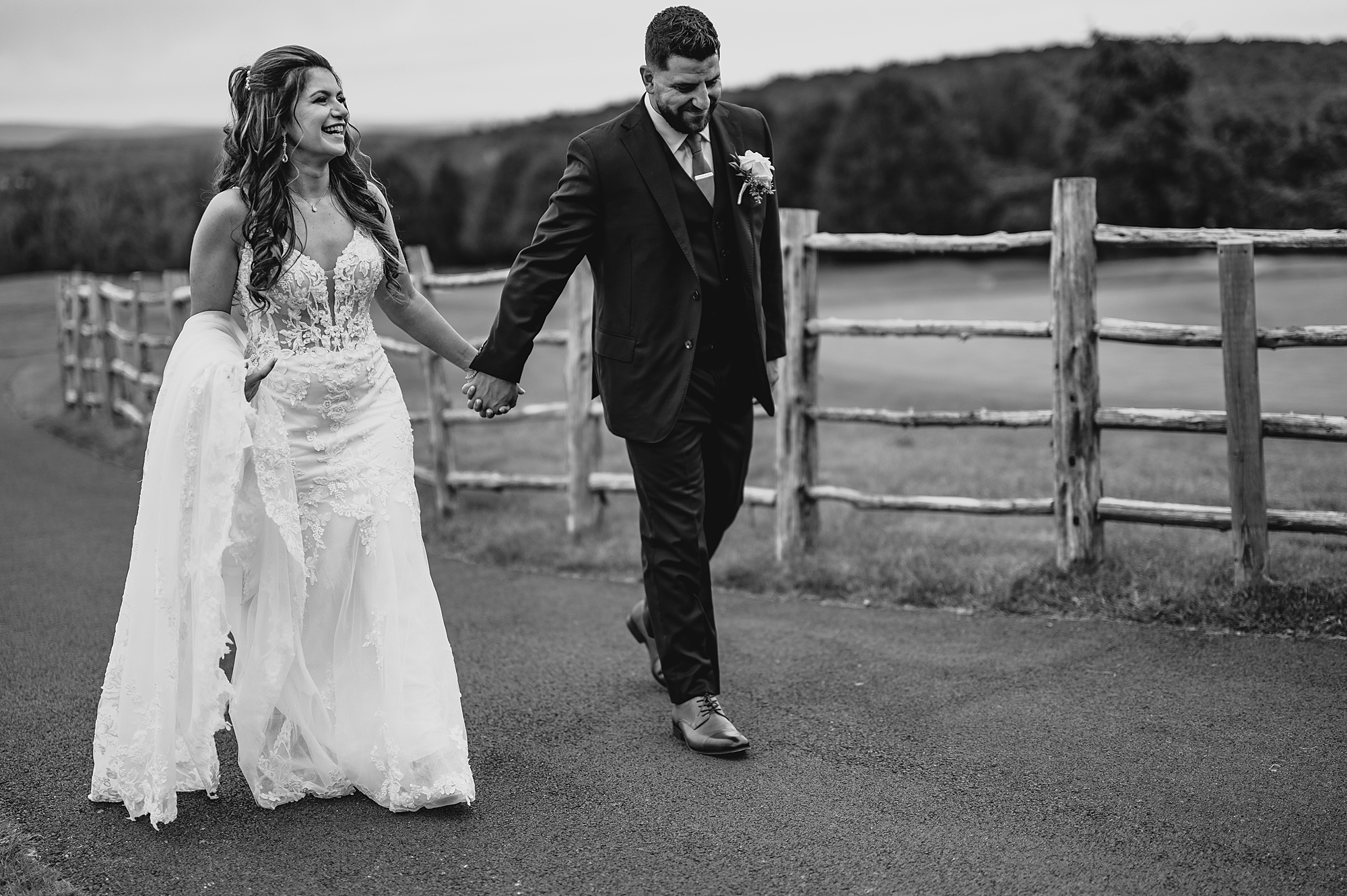 bride and groom hold hands walking along wooden fence