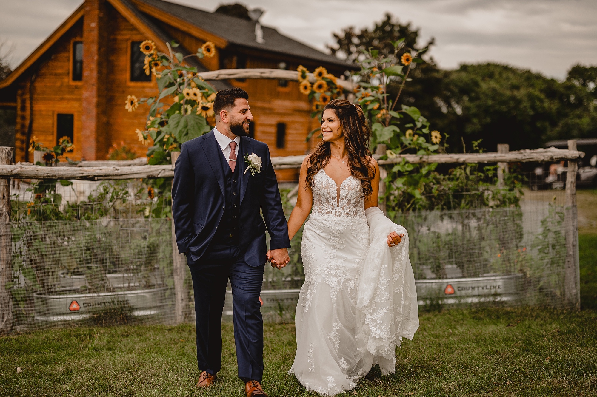 newlyweds hold hands in front of garden boxes with sunflowers