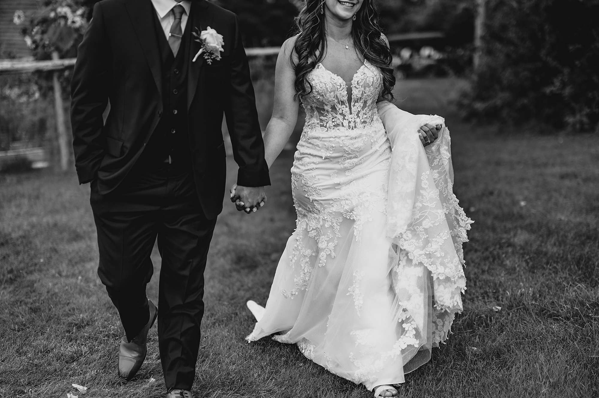 newlyweds hold hands walking while bride holds up skirt of gown