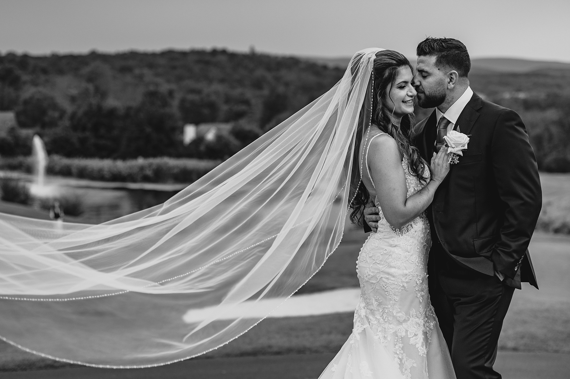 newlyweds hug with bride's veil floating behind them on hill at Skyview Golf Club