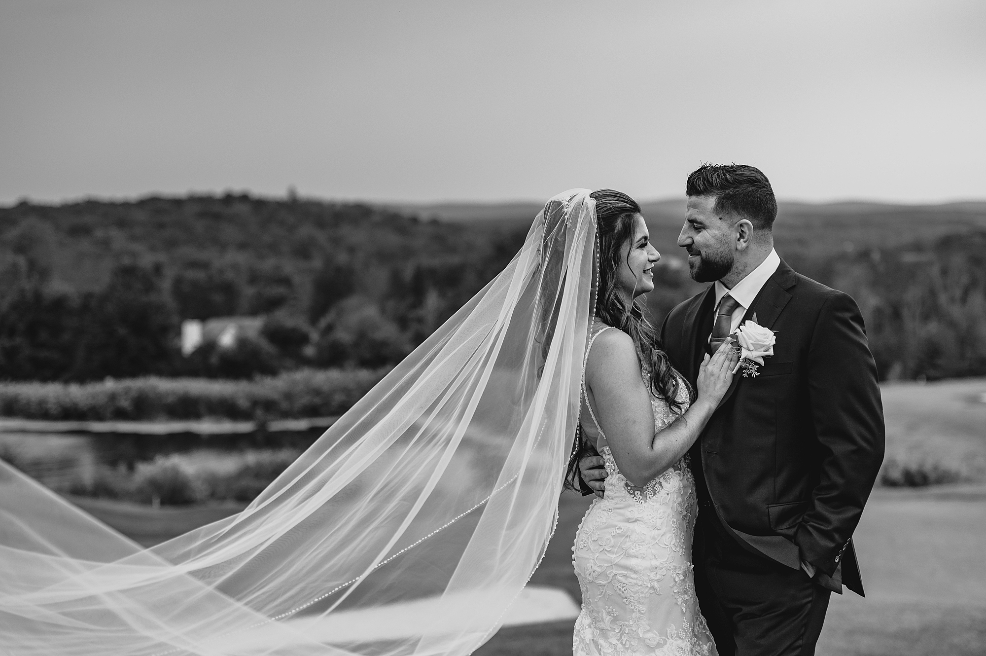 newlyweds hug with bride's veil floating behind them on hill at Skyview Golf Club