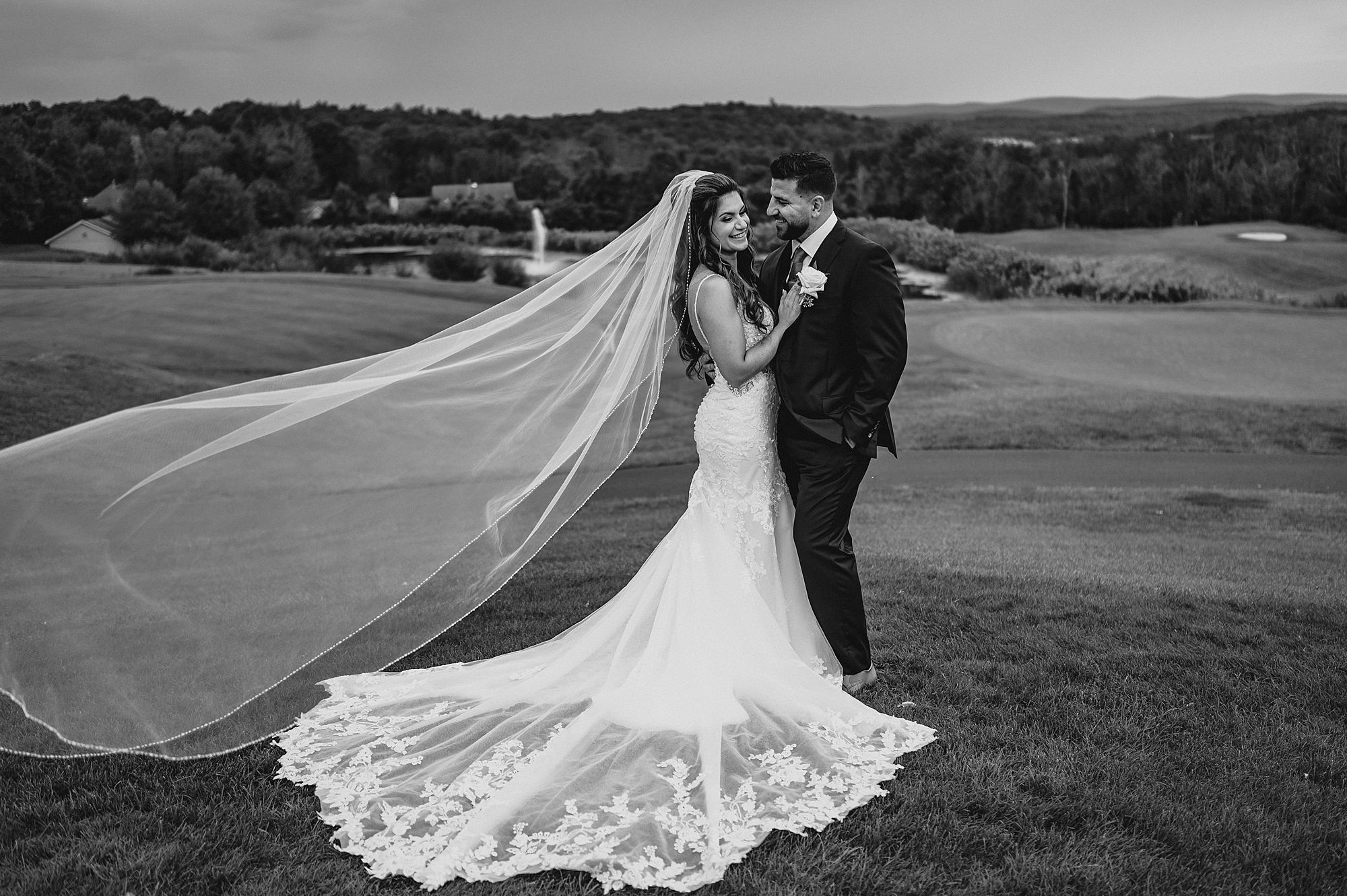 newlyweds hug with bride's veil floating behind them on hill at Skyview Golf Club