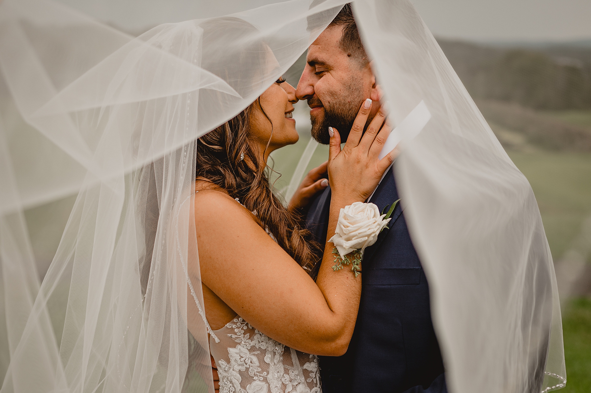 bride and groom lean together under veil on wedding day