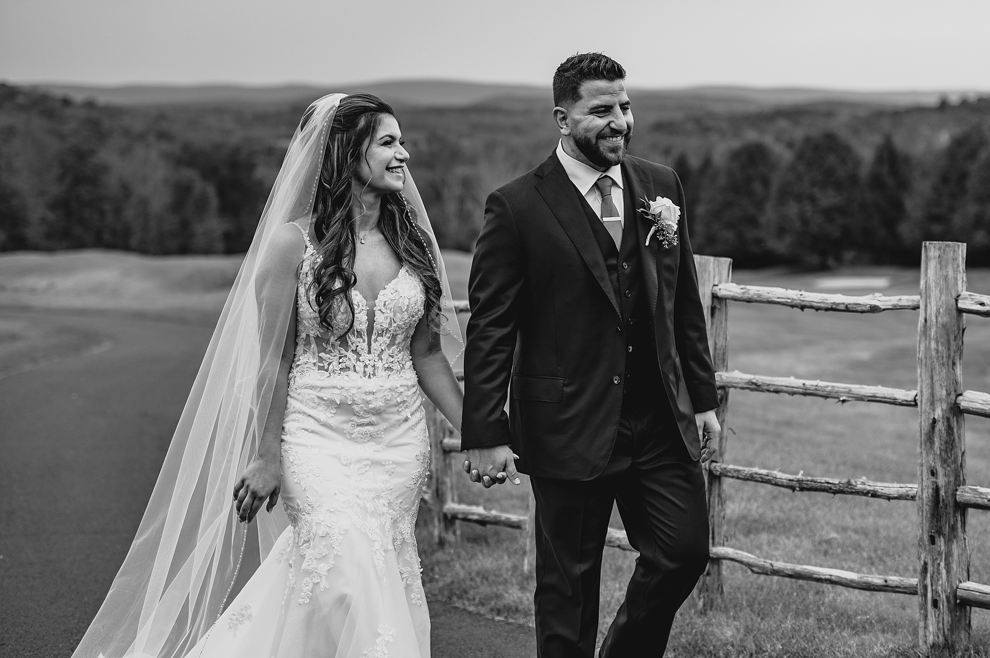 newlyweds hold hands walking along wooden fence at Skyview Golf Club