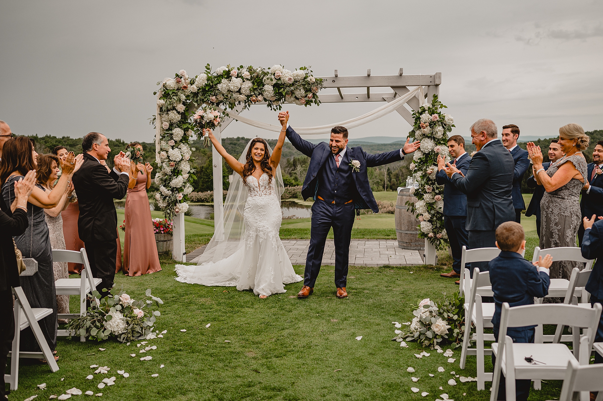 newlyweds hold hands walking away from ceremony on lawn at Skyview Golf Club