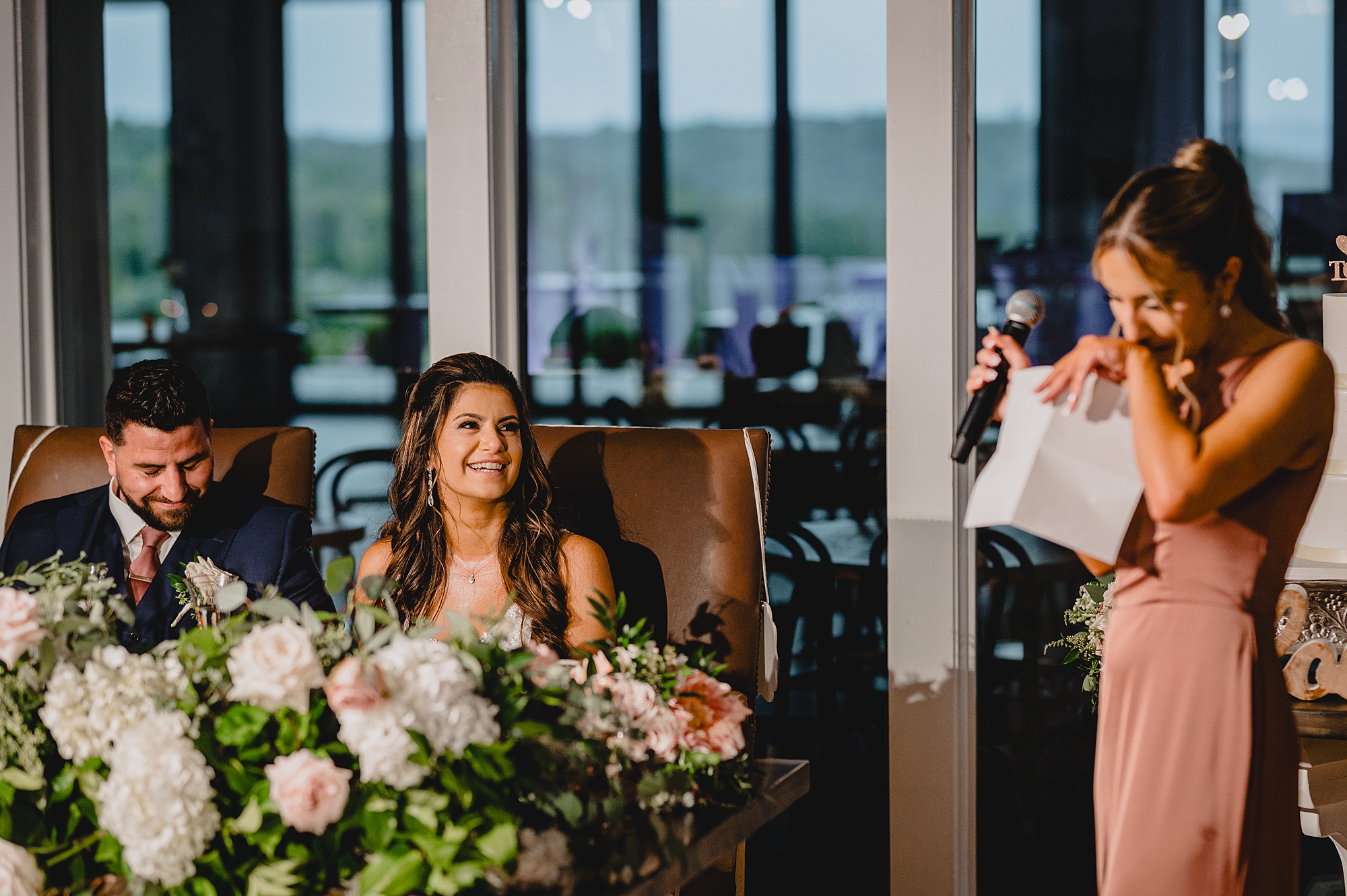 bride listens to bridesmaid give speech during wedding reception