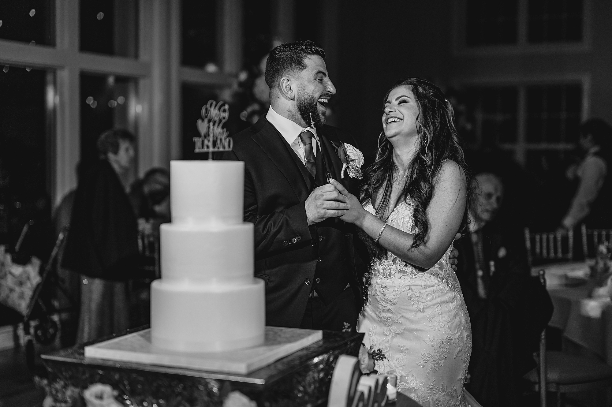 newlyweds laugh standing by wedding cake during NJ wedding reception